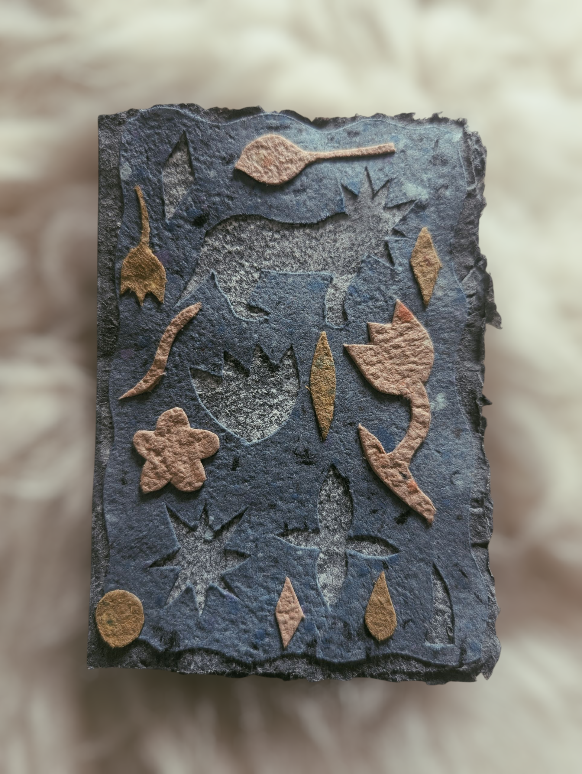 Fossil mit Reliefabbildung eines Einhorns, umgeben von Blumen- und Sternmotiven auf schwarzem Stein.