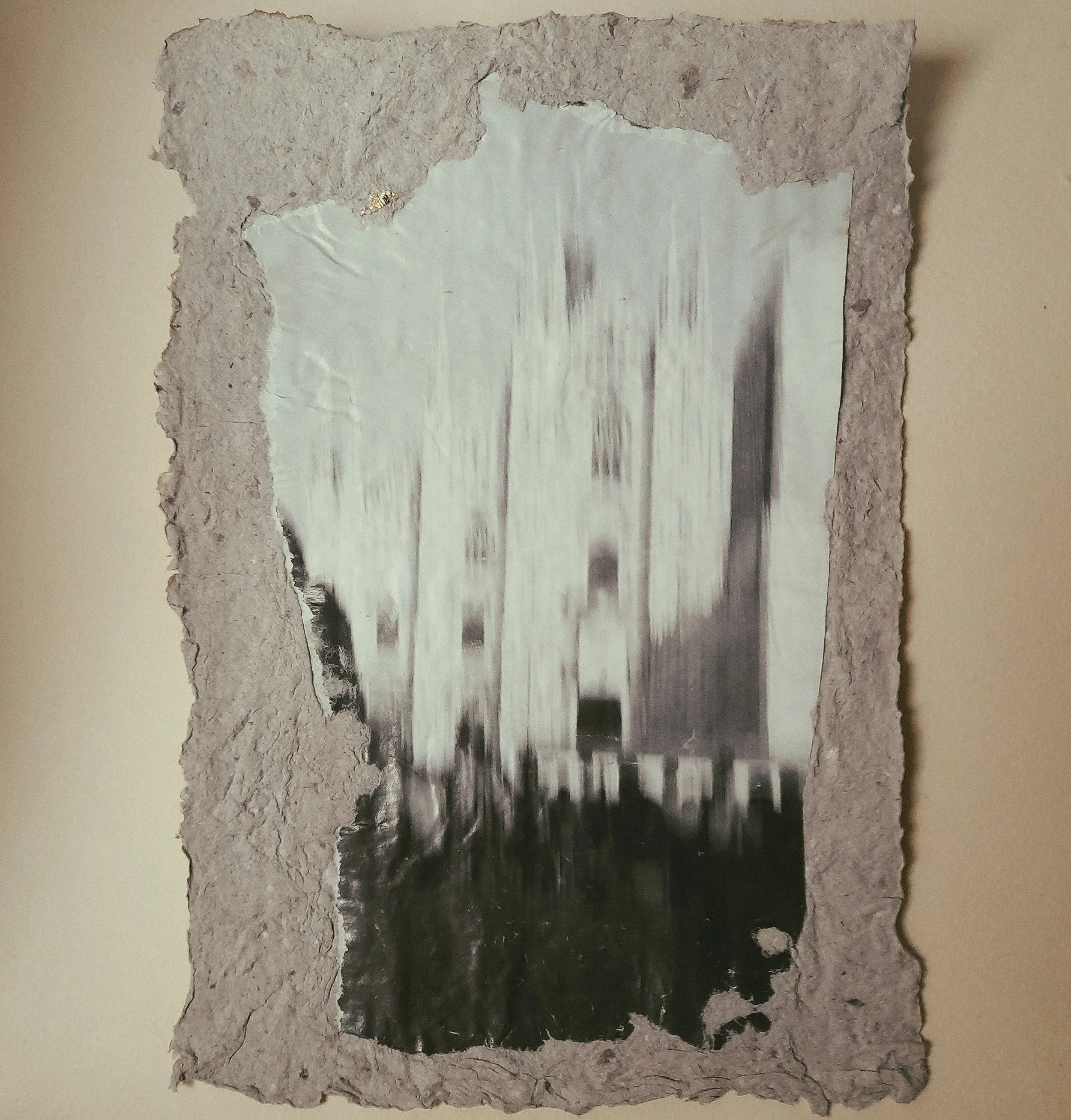 Schwarz-weiß-Foto eines Gebäudes, das an einer Wand hängt, umrandet von zerknittertem, grauem Papier.