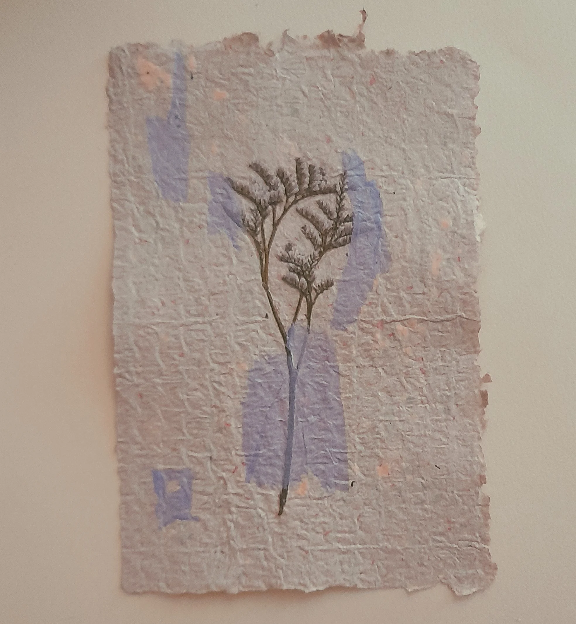 Eine getrocknete Pflanze auf einem handgemachten Papier mit blauen Verzierungen.