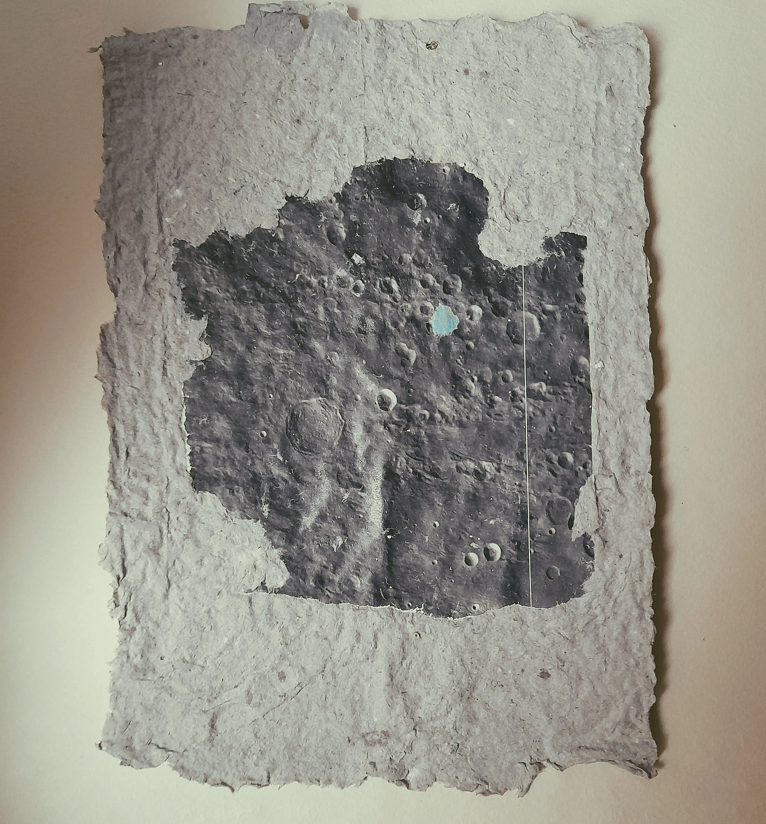 Schwarz-weiß-Foto des Mondes auf einem rauen, unregelmäßig geformten Papierstück, an einer Wand befestigt.