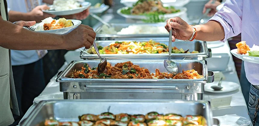 Chafing trays of food are shown, with multiple people plating food from them using metal servingware.