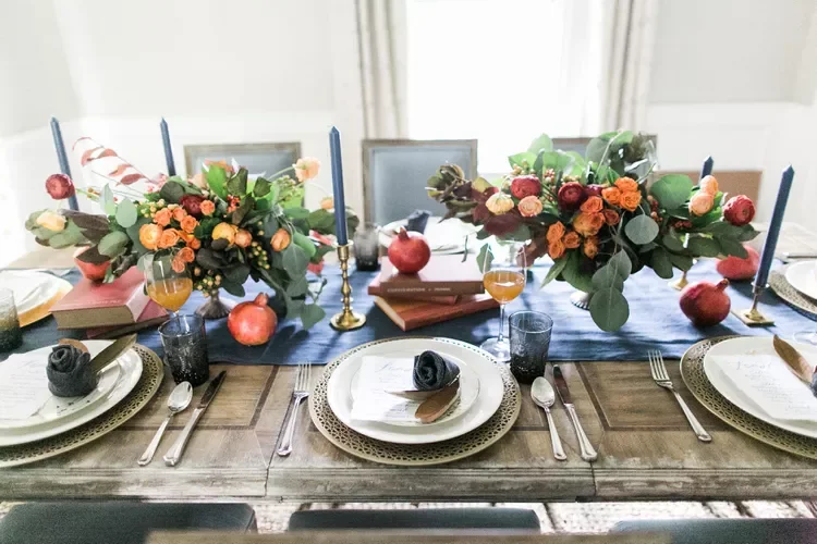 A place setting for 6 with white plates is shown. On the table are bouquets of red, orange, yellow, and deep blue flowers. Blue candles are shown.