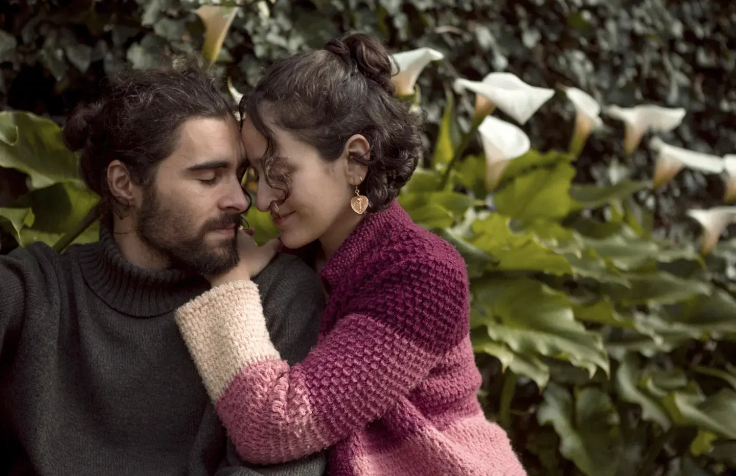 A bearded man and a woman embrace in front of a natural backdrop.