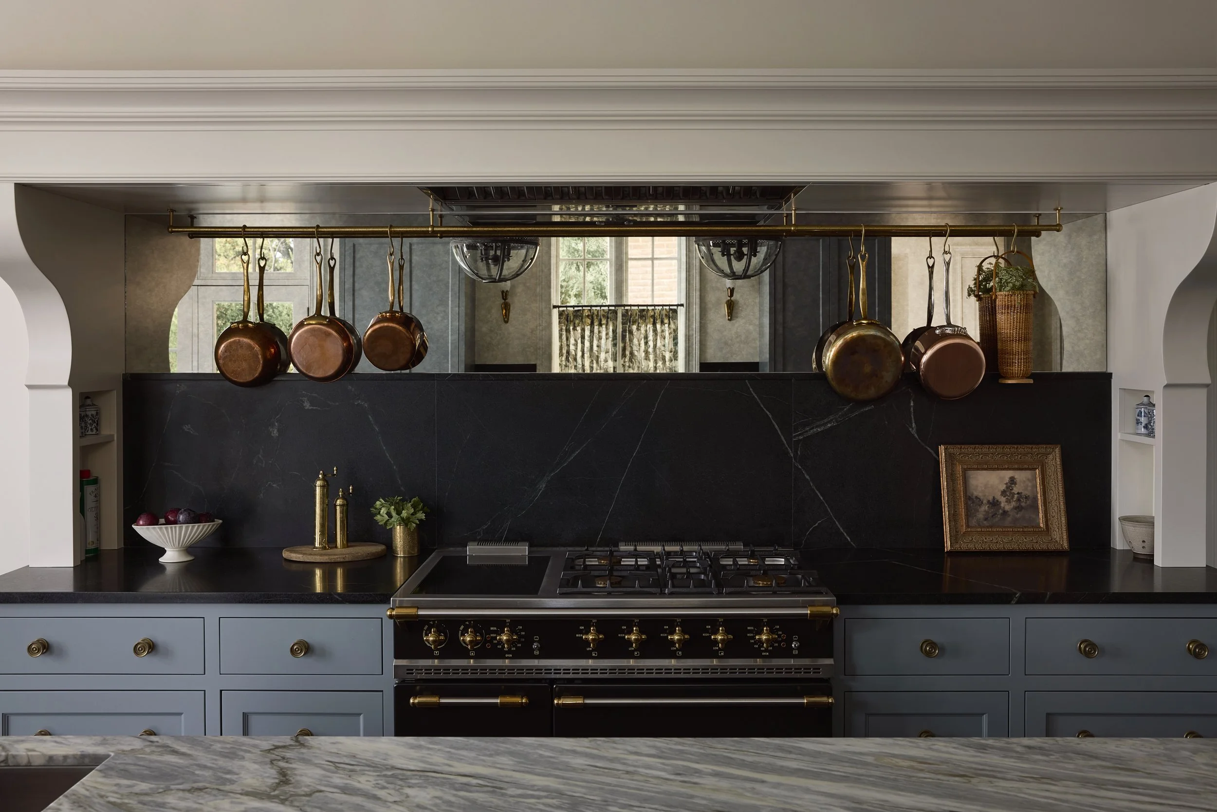 A traditional style kitchen with blue cabinetry and mirrored backsplash
