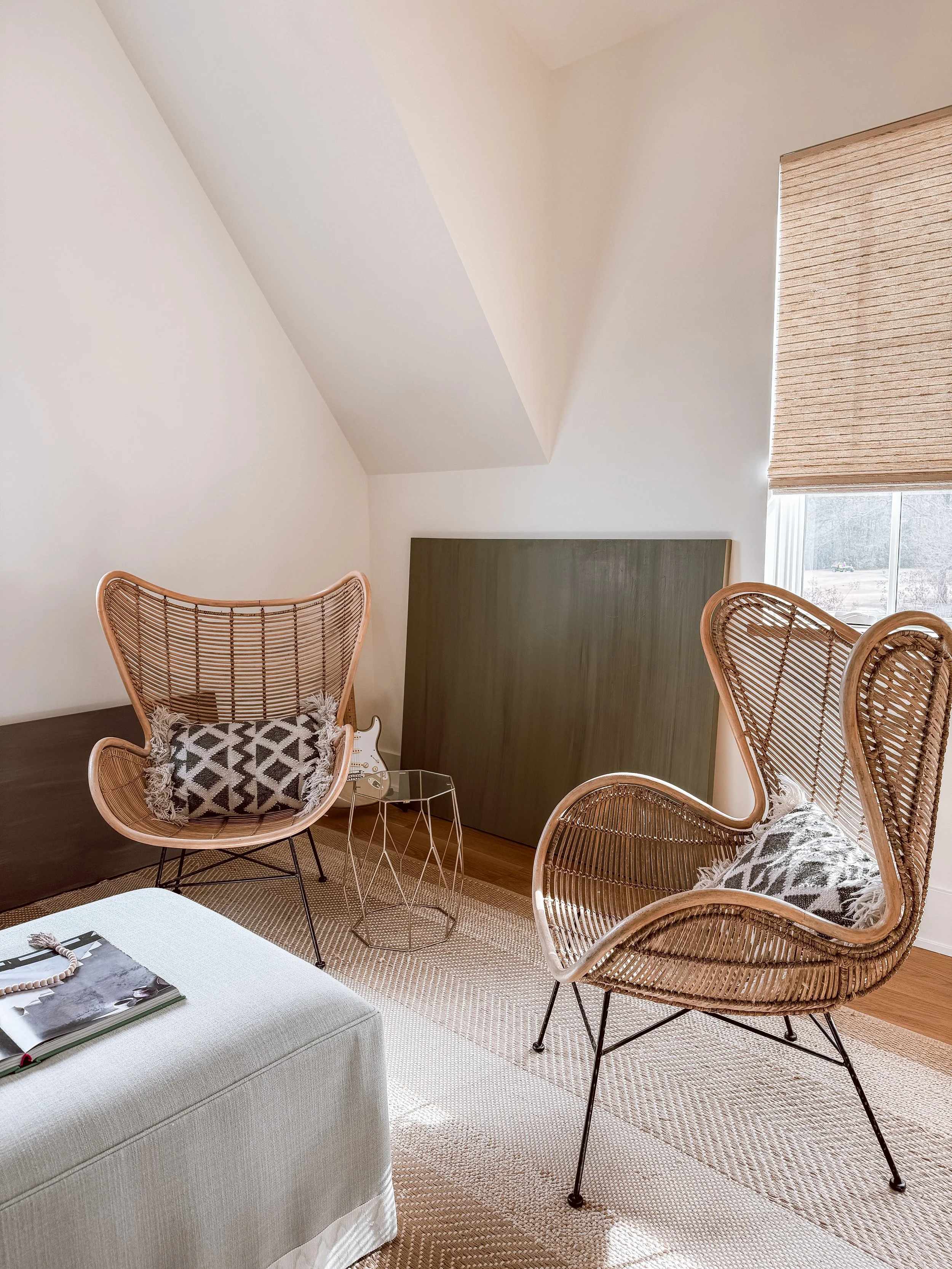 Two rattan egg-shaped chairs in Christie Raju’s studio with a large green abstract painting in the background, highlighting a serene and minimal workspace.
