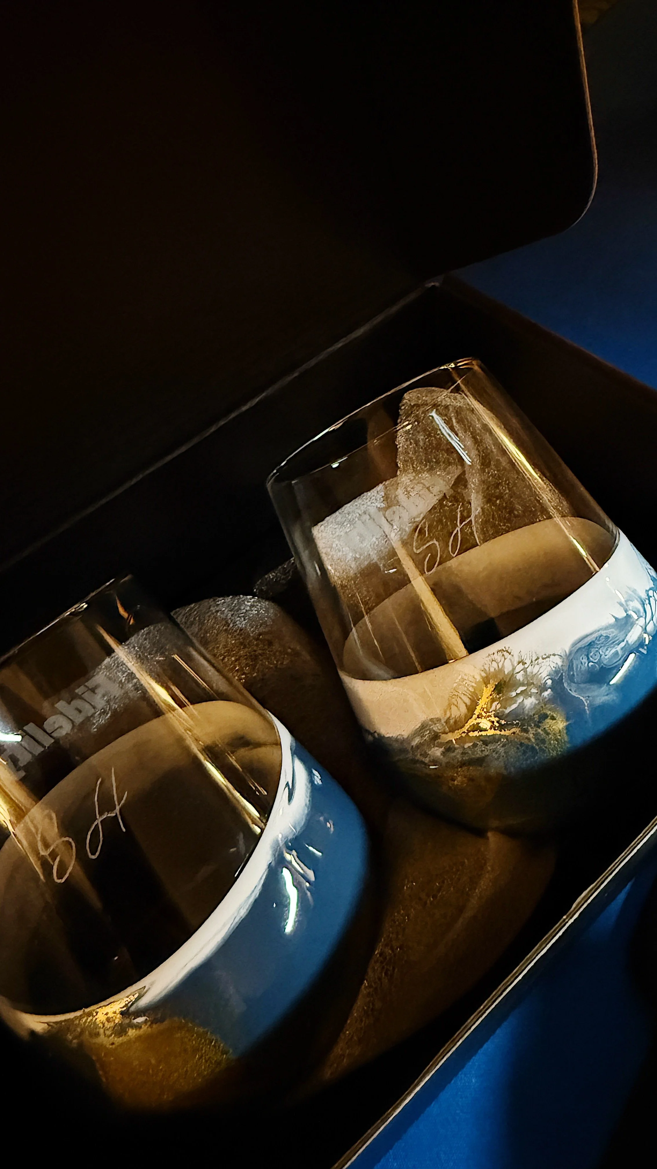 A close-up of champagne glasses with ice and a champagne bottle inside a black box, with reflections on the glasses.