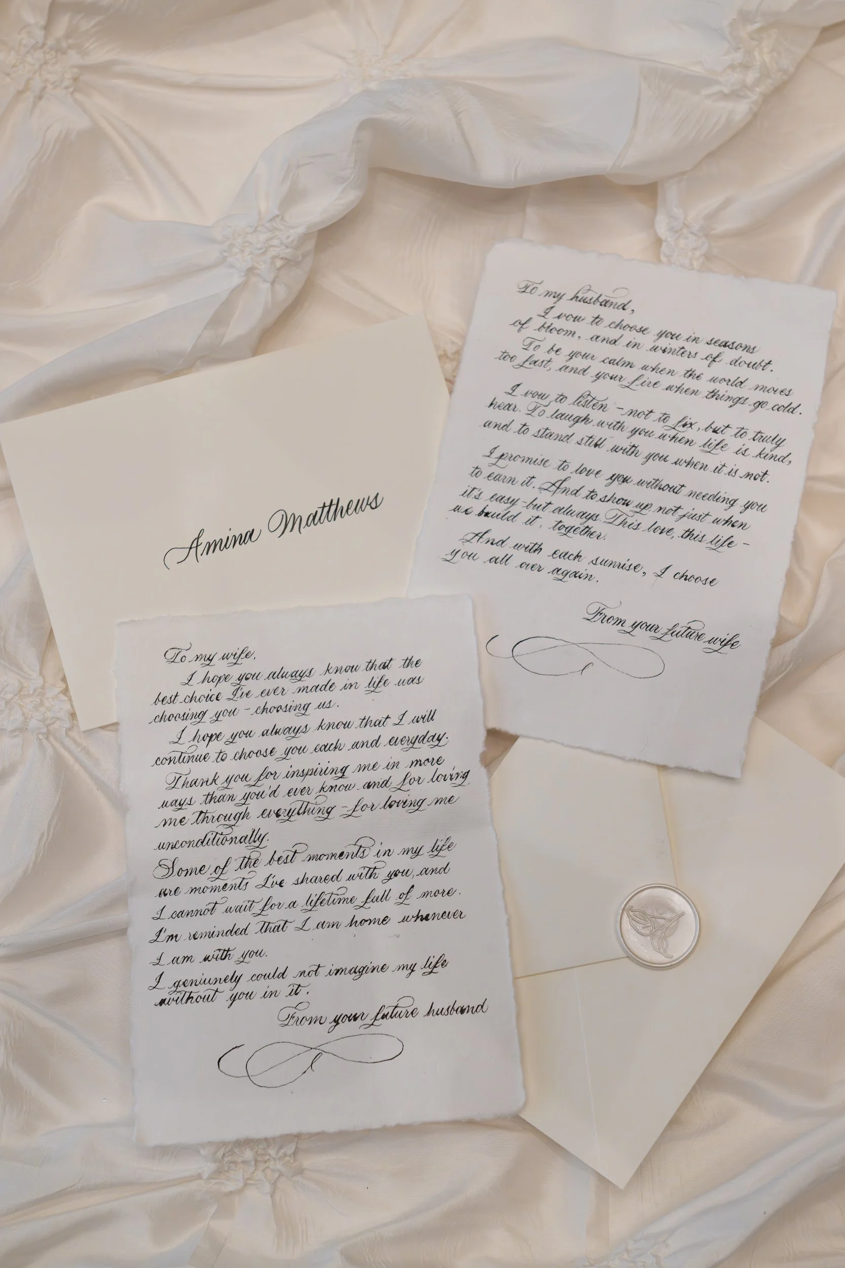 Several sheets of handwritten love letters or notes on textured, cream-colored fabric with decorative stitching and a metallic coin or token.