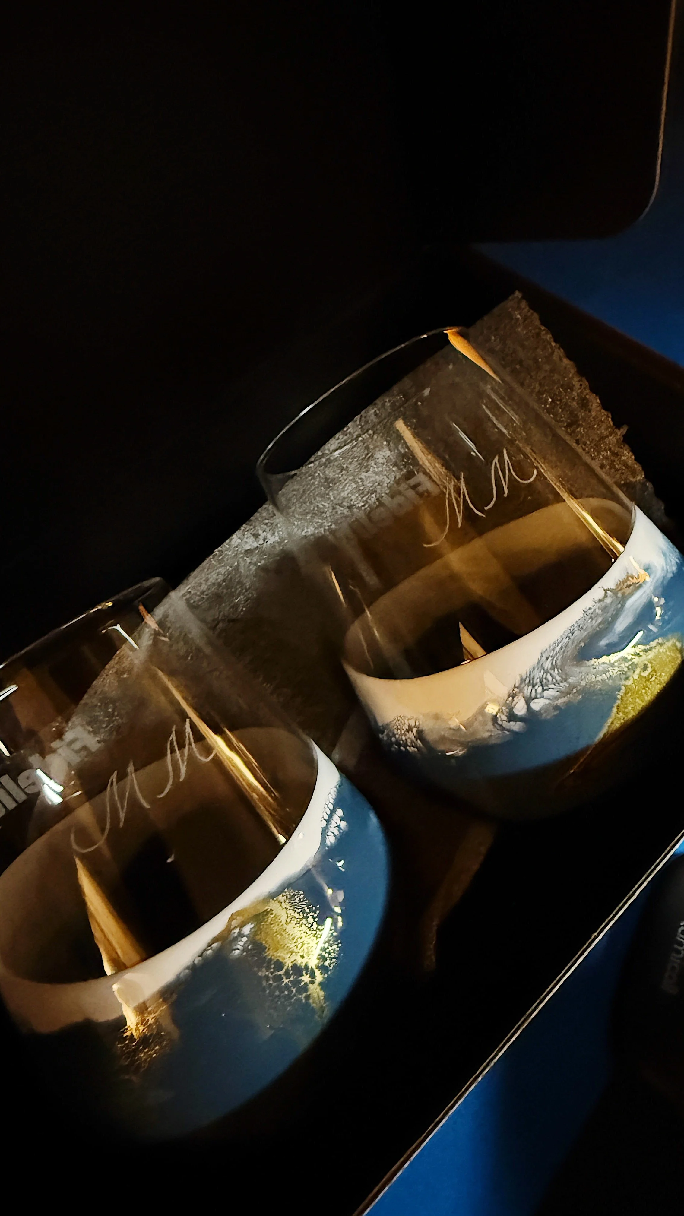Two glasses of dark beer with foam on top, placed on a black tray with foam residue on the rims, and a black napkin underneath, against a dark background.