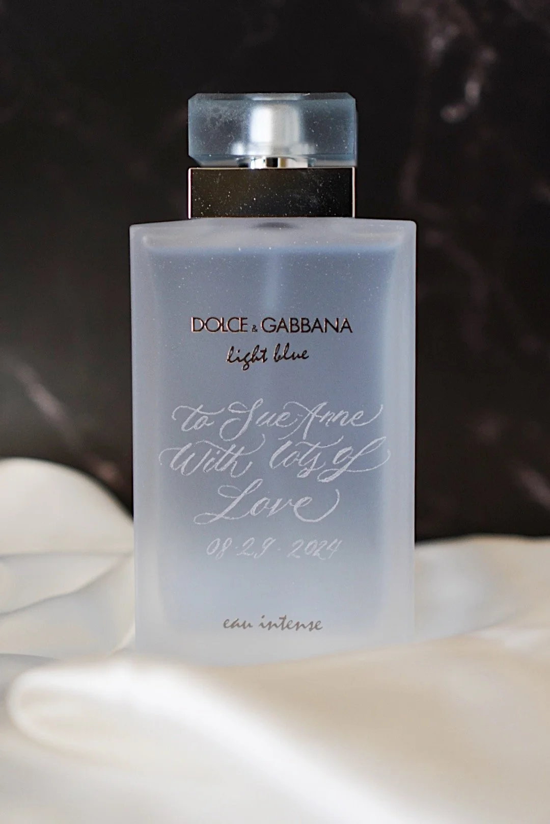 A bottle of Dolce & Gabbana Light Blue perfume on a white fabric background with soft lighting.