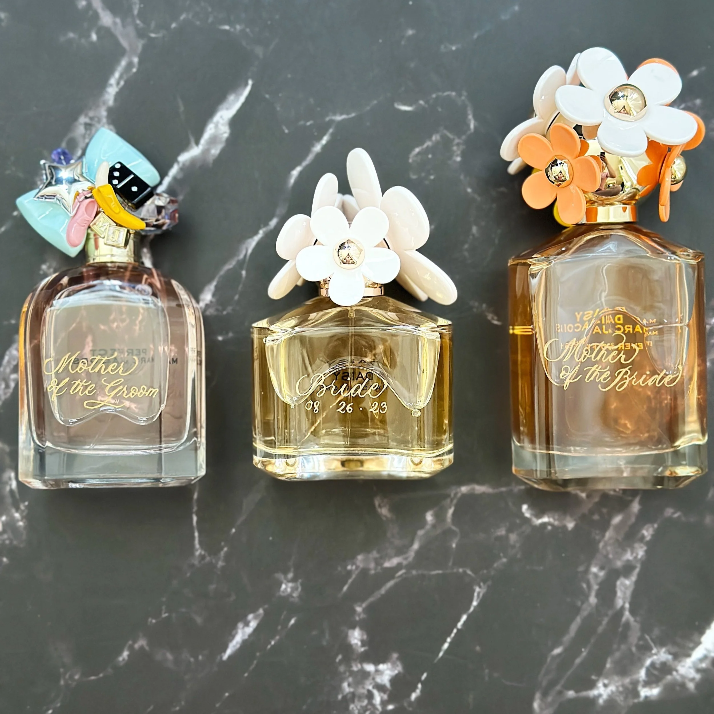 Close-up of perfume bottles with flower-shaped caps on a black marble surface.