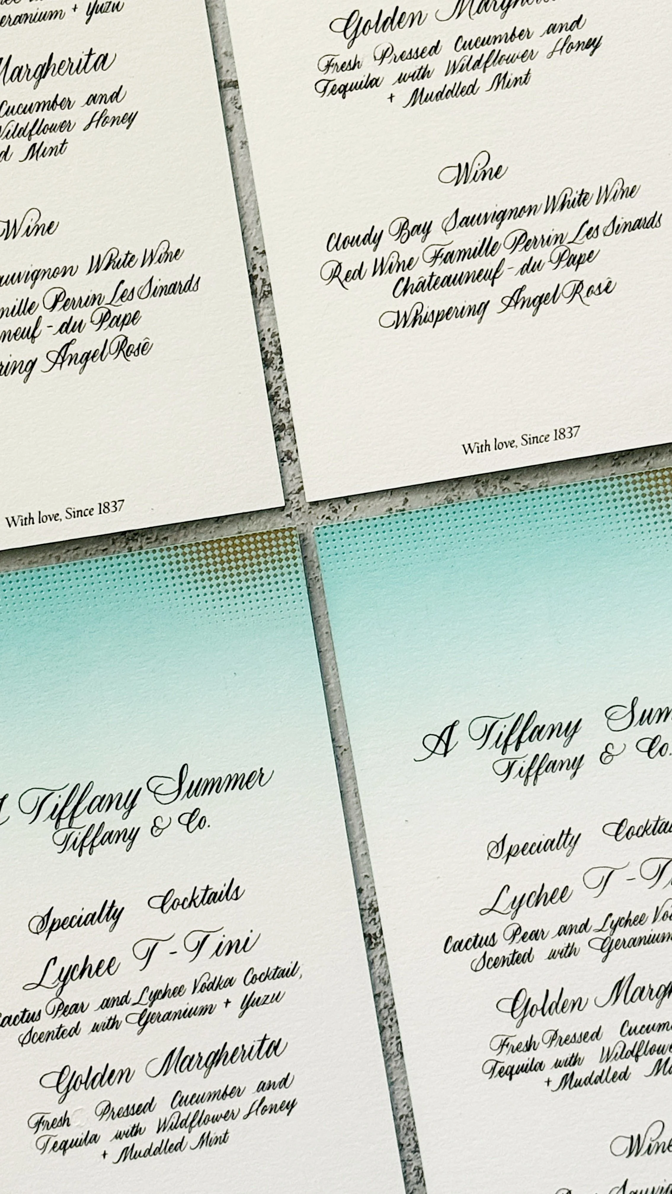 Close-up of printed menu cards featuring cocktails and wine options, including ingredients and descriptions, with elegant cursive font on textured paper.