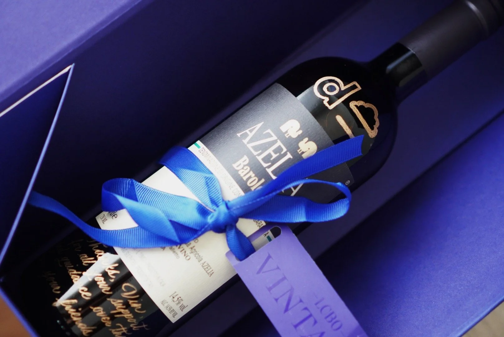 A bottle of Barolo wine with a blue ribbon and card, inside a blue box.