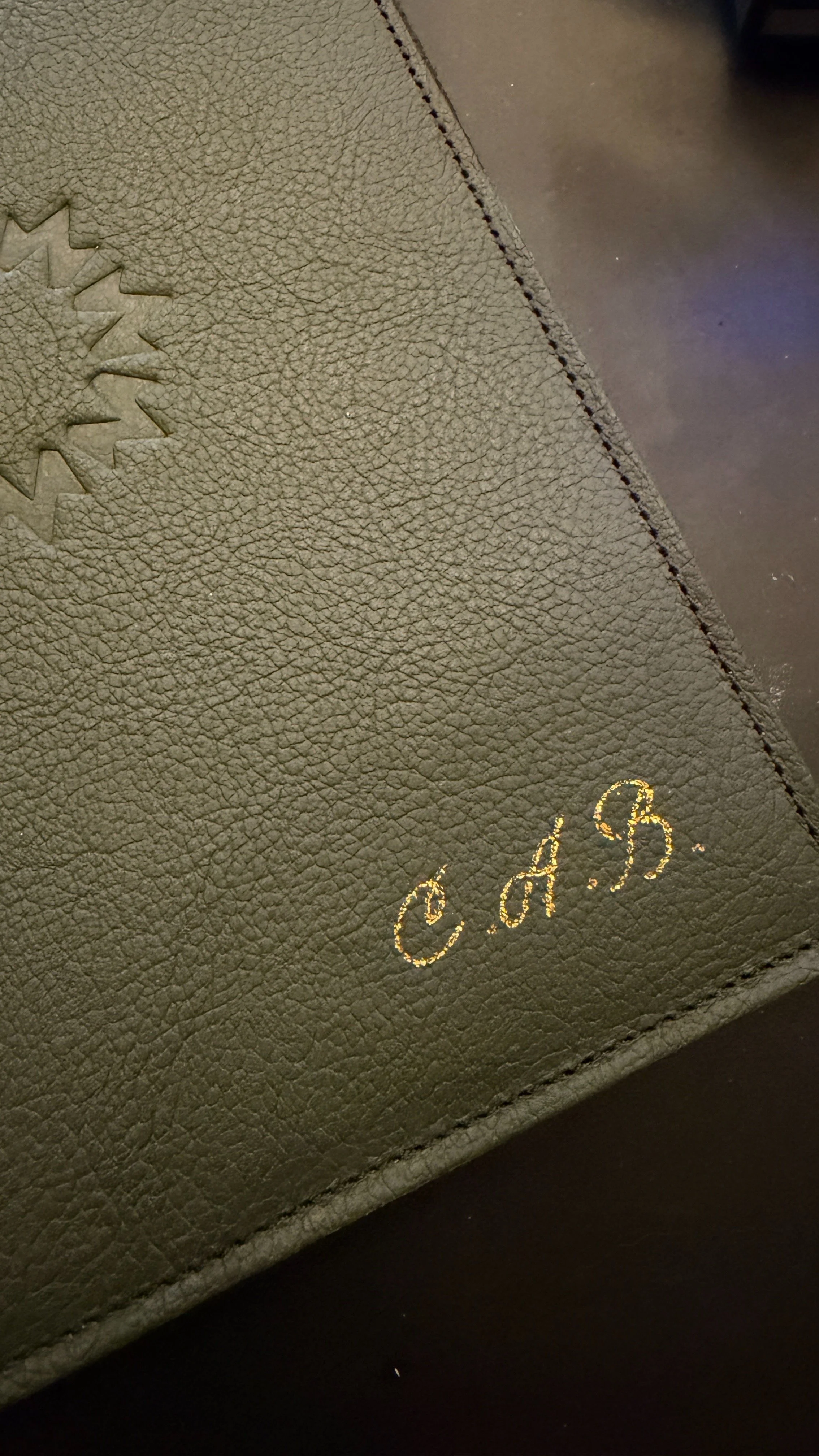 Close-up of a beige textured surface with a stitched seam and gold embossed initials 'C.A.B'.