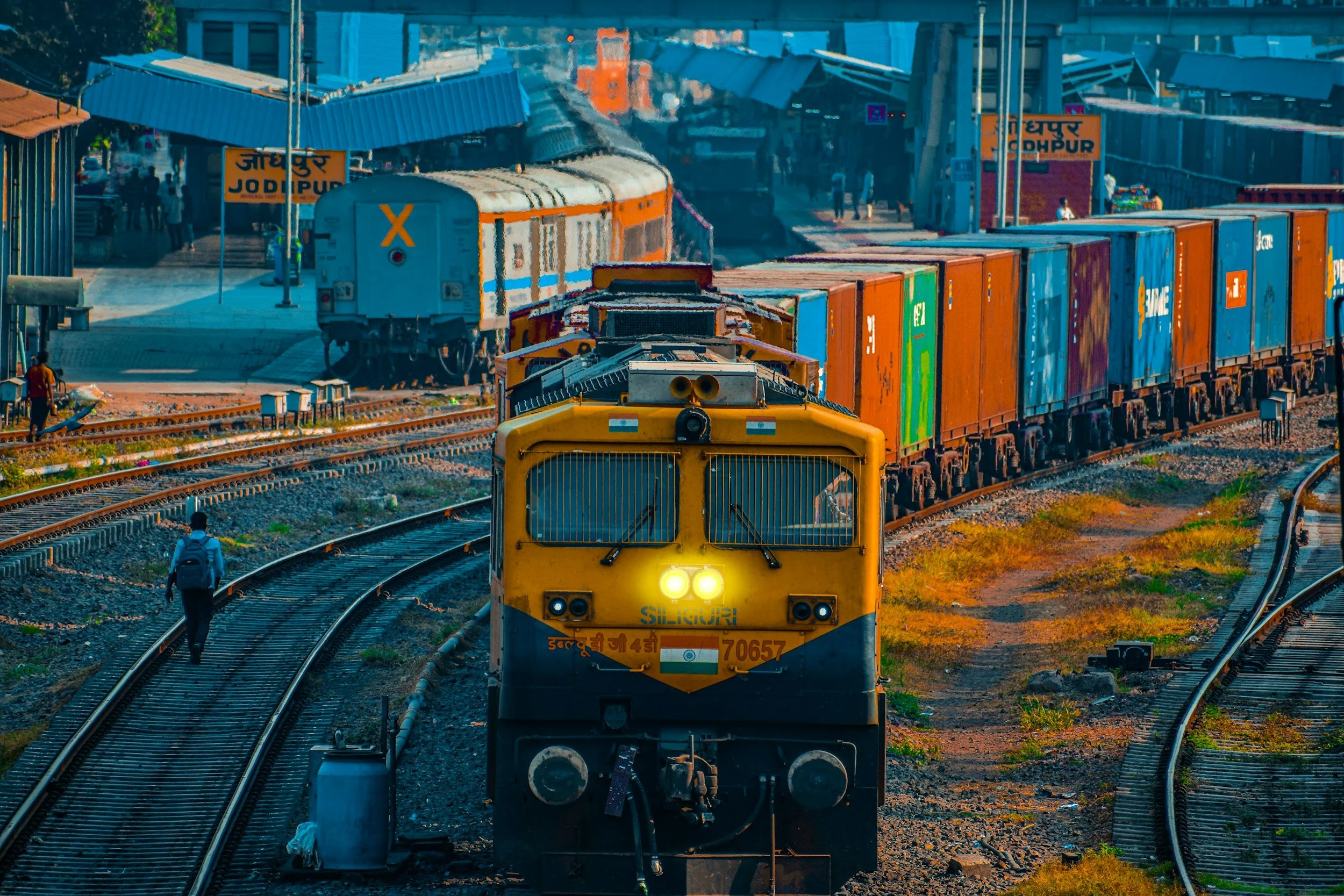 Un train de marchandises arrive sur les rails avec des conteneurs colorés en arrière-plan à la gare de Jodhpur, en Inde, en plein jour.