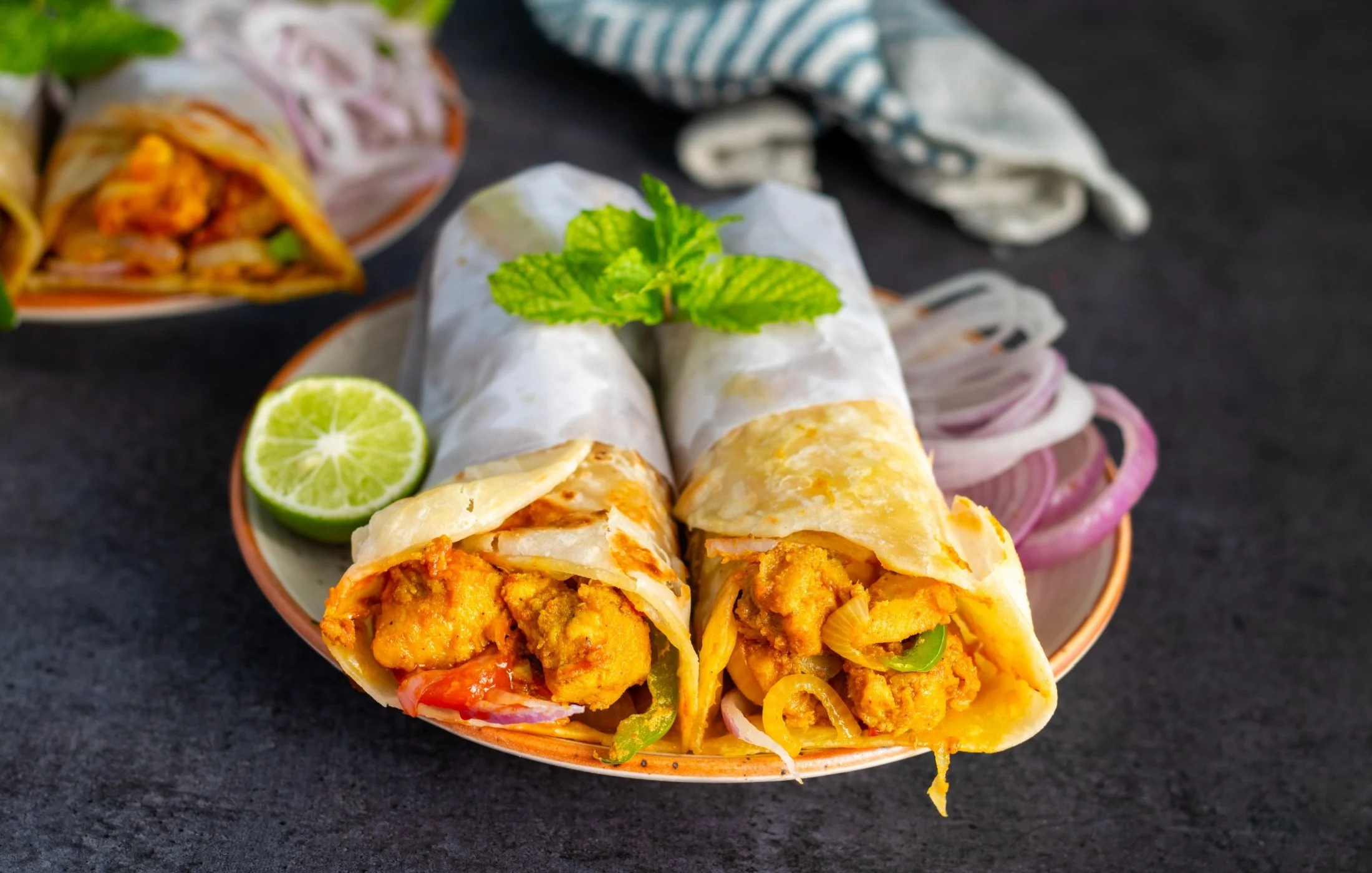 Fresh chicken kathi rolls filled with grilled chicken, onions, peppers, and spices, served with lime and fresh mint on a plate.