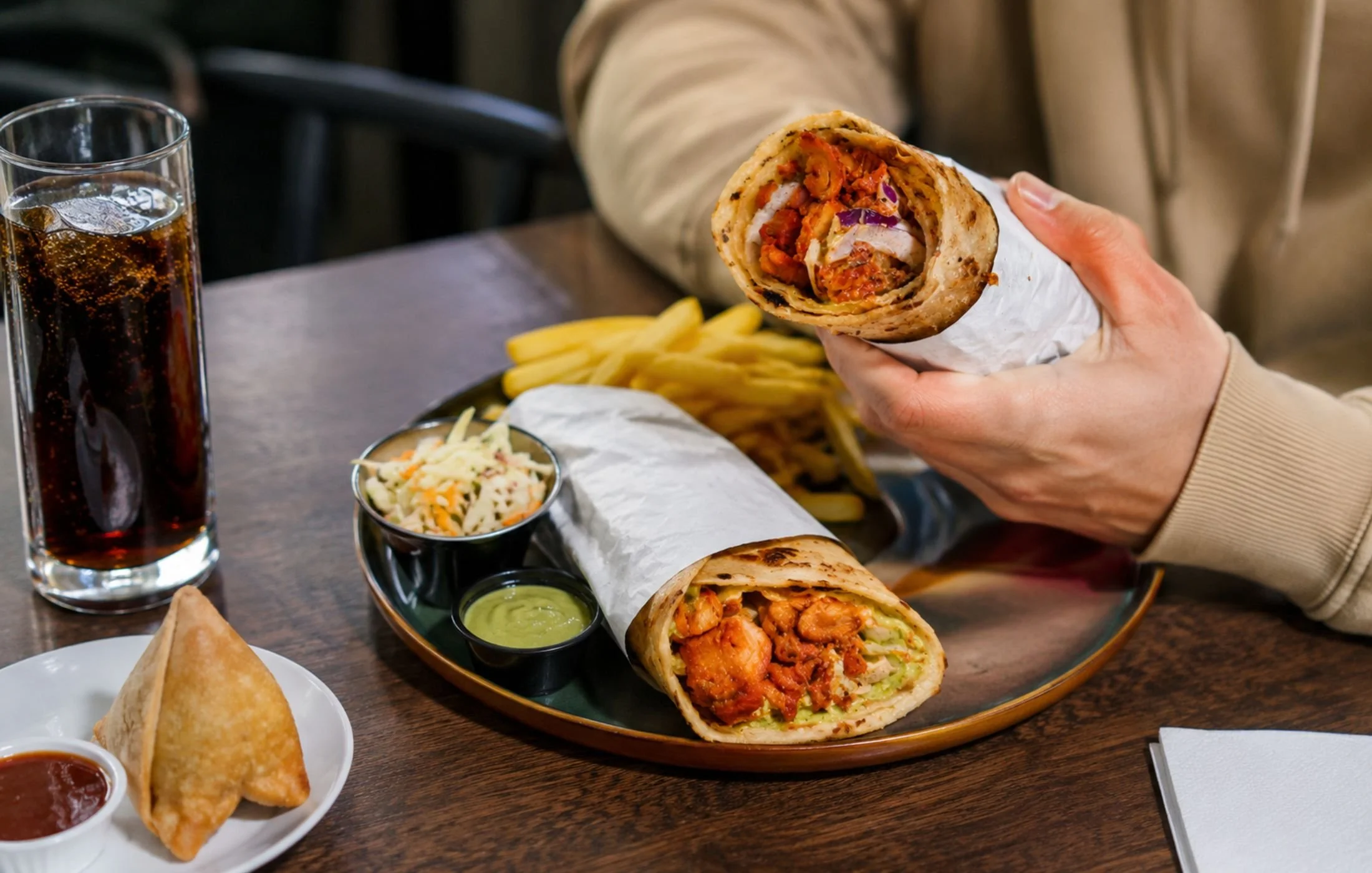 Chicken kathi rolls served with fries, samosa, mint chutney and a cold drink at an Indian street food restaurant in Canada.