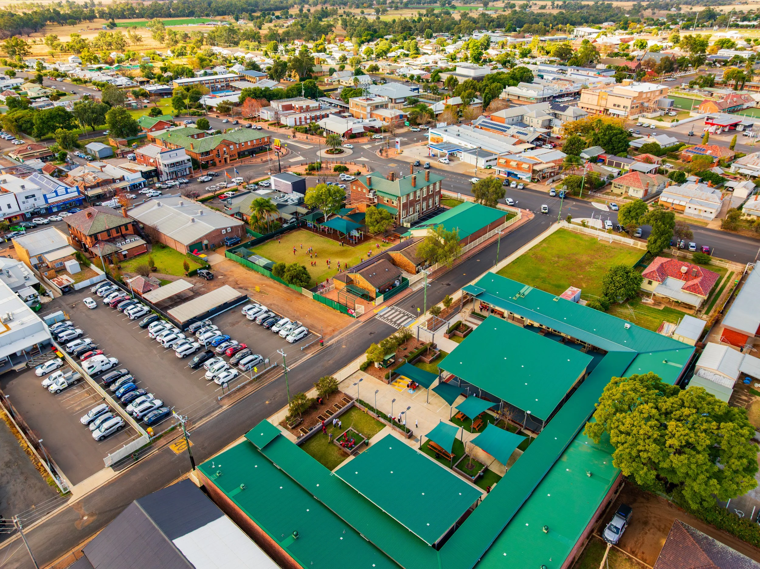 An aerial view of Carinya Christian School, Gunnedah, located in a small town, shows various buildings, parking lots, green spaces, and streets with trees and cars.