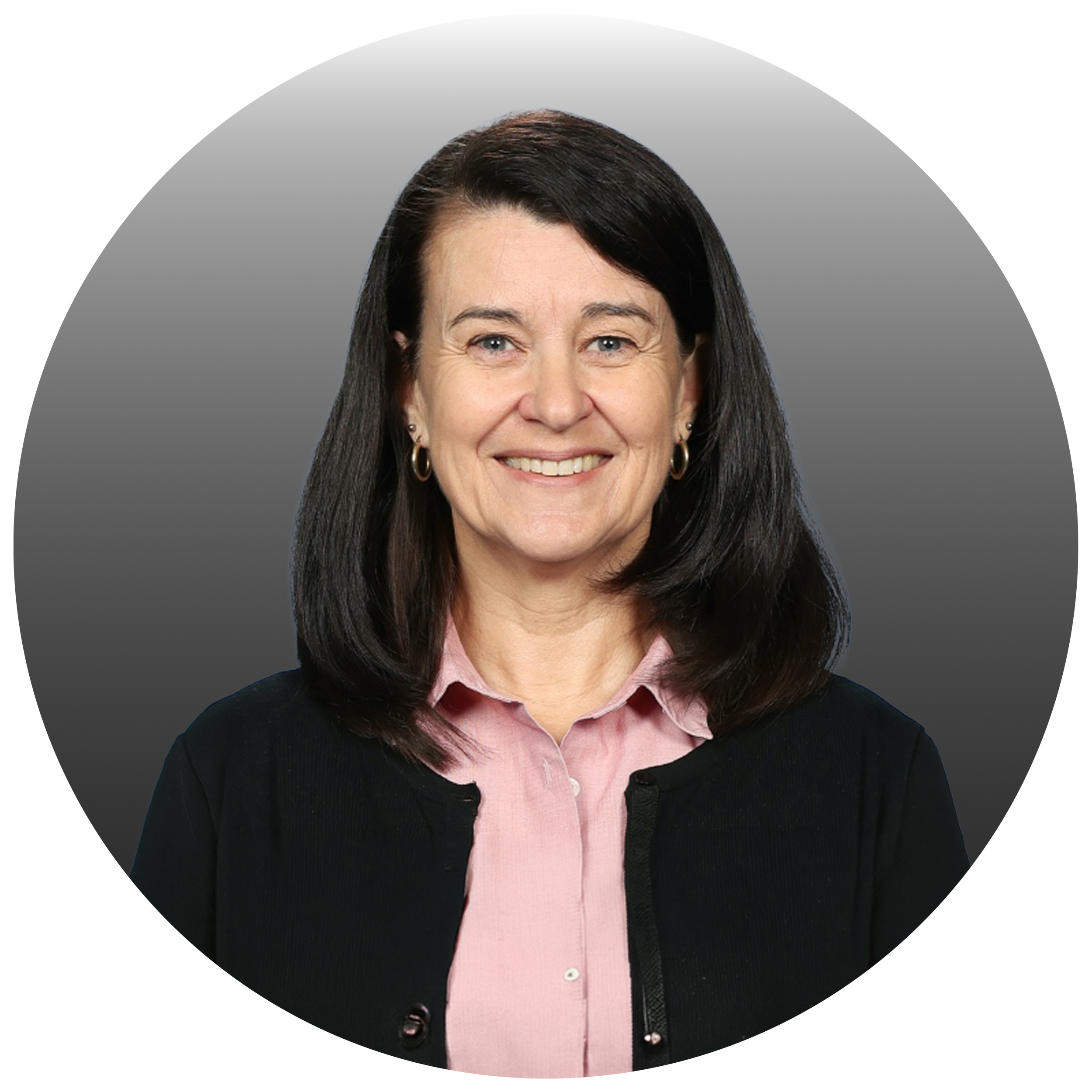 Photograph of a smiling middle-aged woman with dark hair, wearing a pink shirt and black blazer, against a gray gradient background.