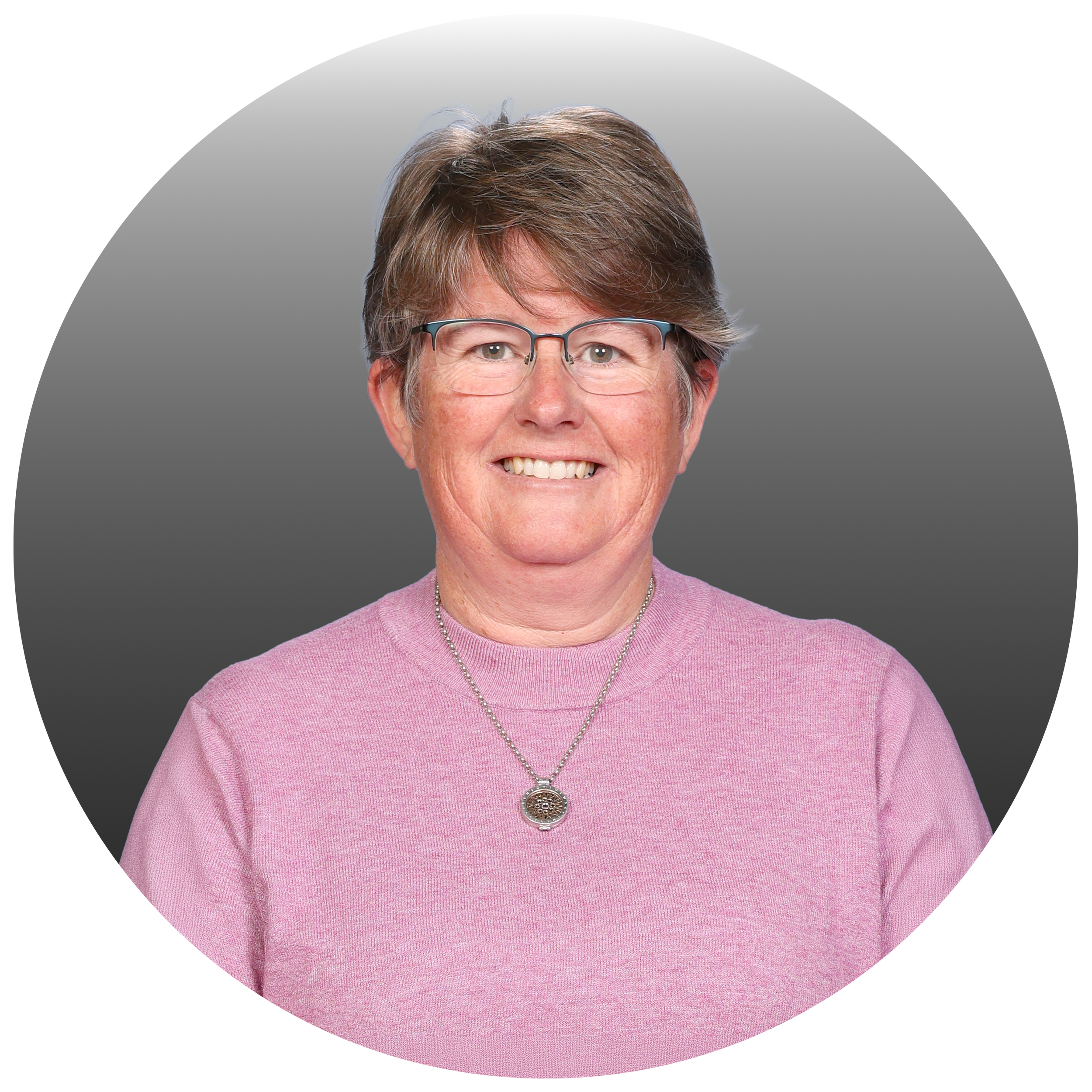 Portrait of a smiling woman with short brown hair, glasses, wearing a pink sweater and a silver necklace with a round pendant.