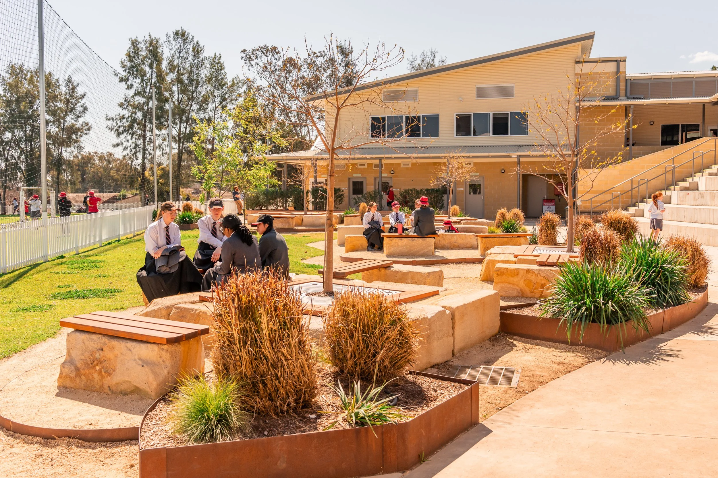 Carinya students in school uniforms sitting on benches and talking outside in the Senior School courtyard at Carinya Christian School, Tamworth.