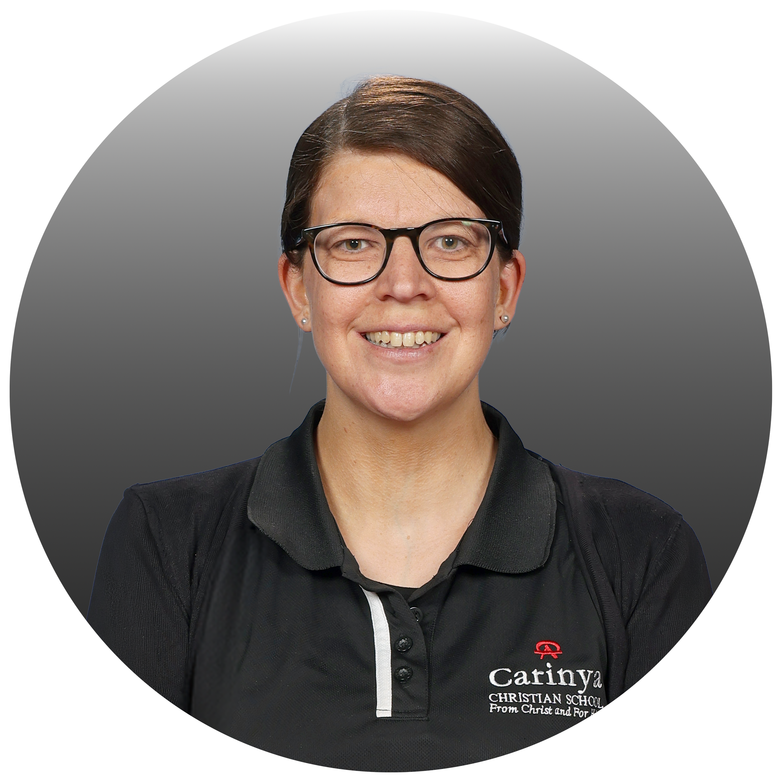 A woman wearing glasses and a black polo shirt with the logo and name "Carinya Christian School" smiling at the camera.