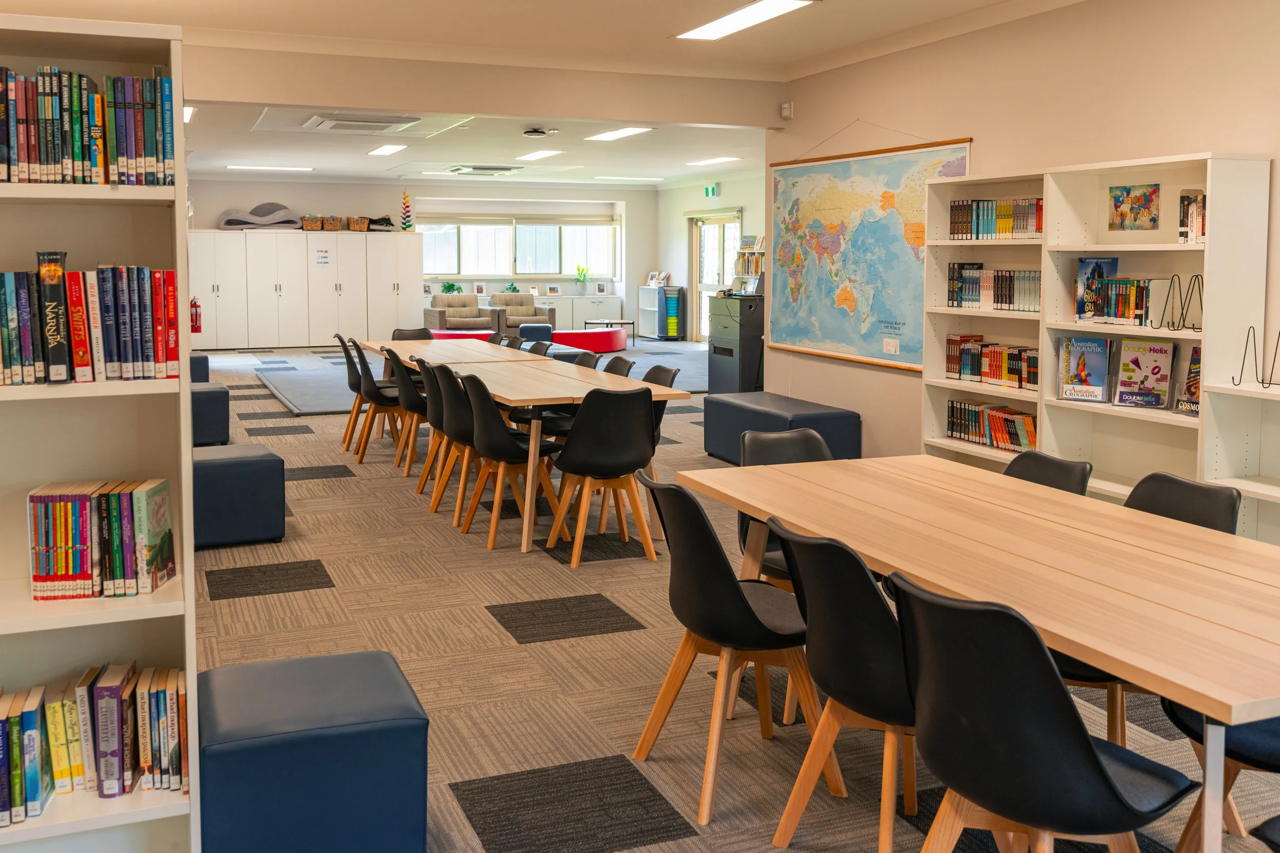 A library or study room with bookshelves, tables, and chairs, featuring a world map on the wall.
