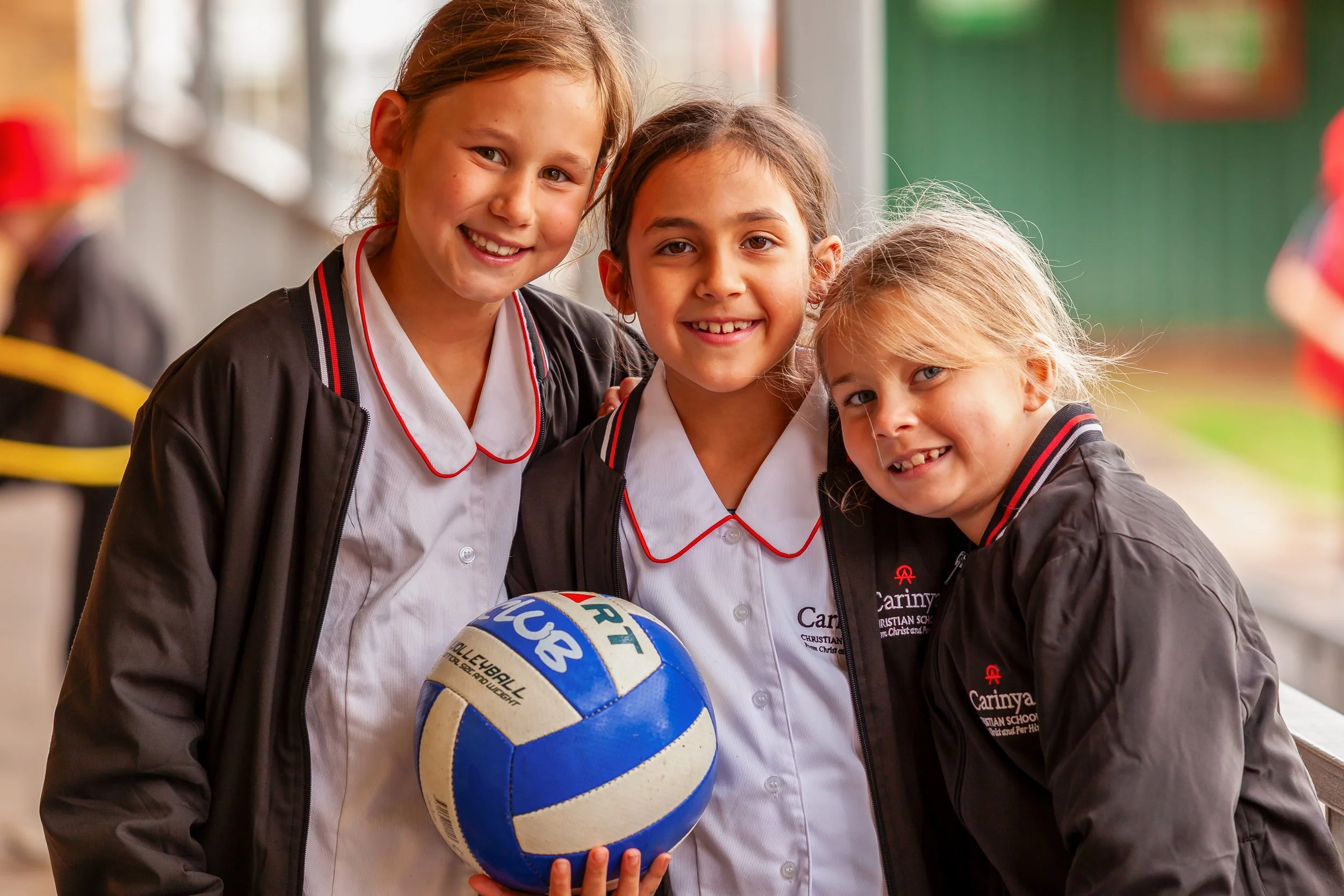 Three young girls in school uniforms smiling and holding a volleyball