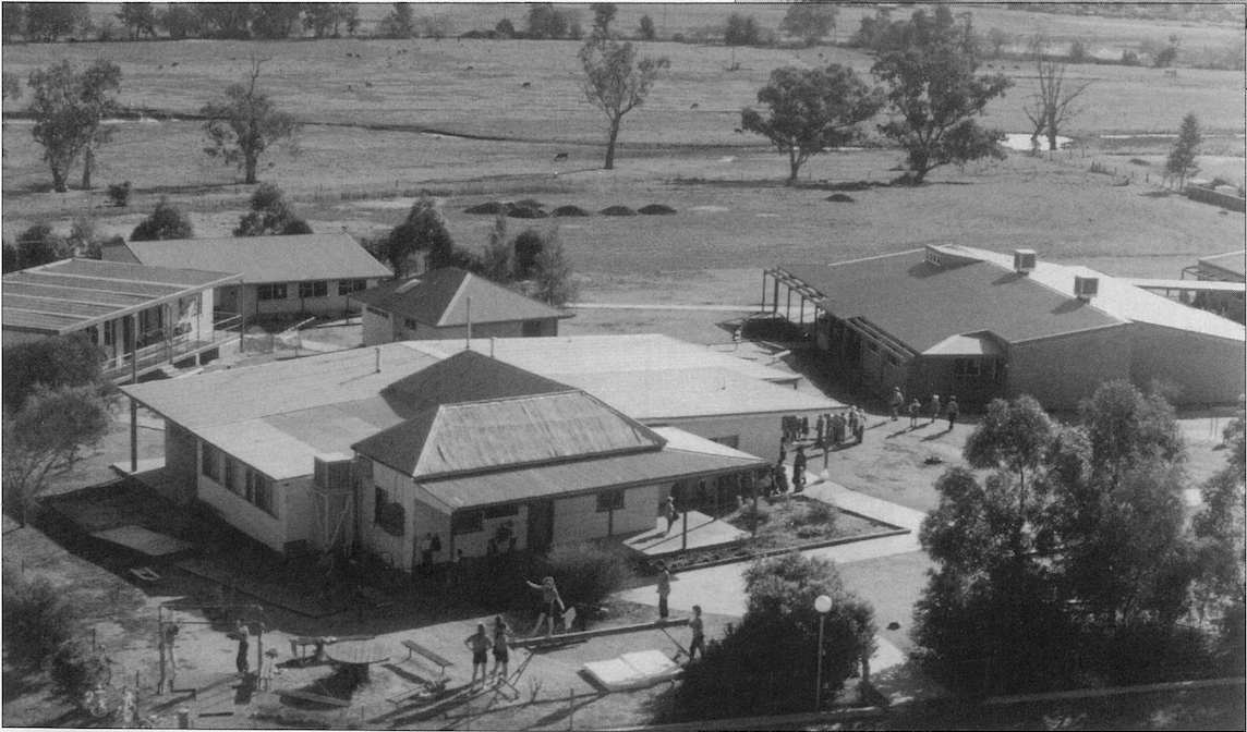 Carinya Christian School Historical photos, Black and white aerial view of a school campus with multiple buildings, children playing outside, trees, and open field in the background.