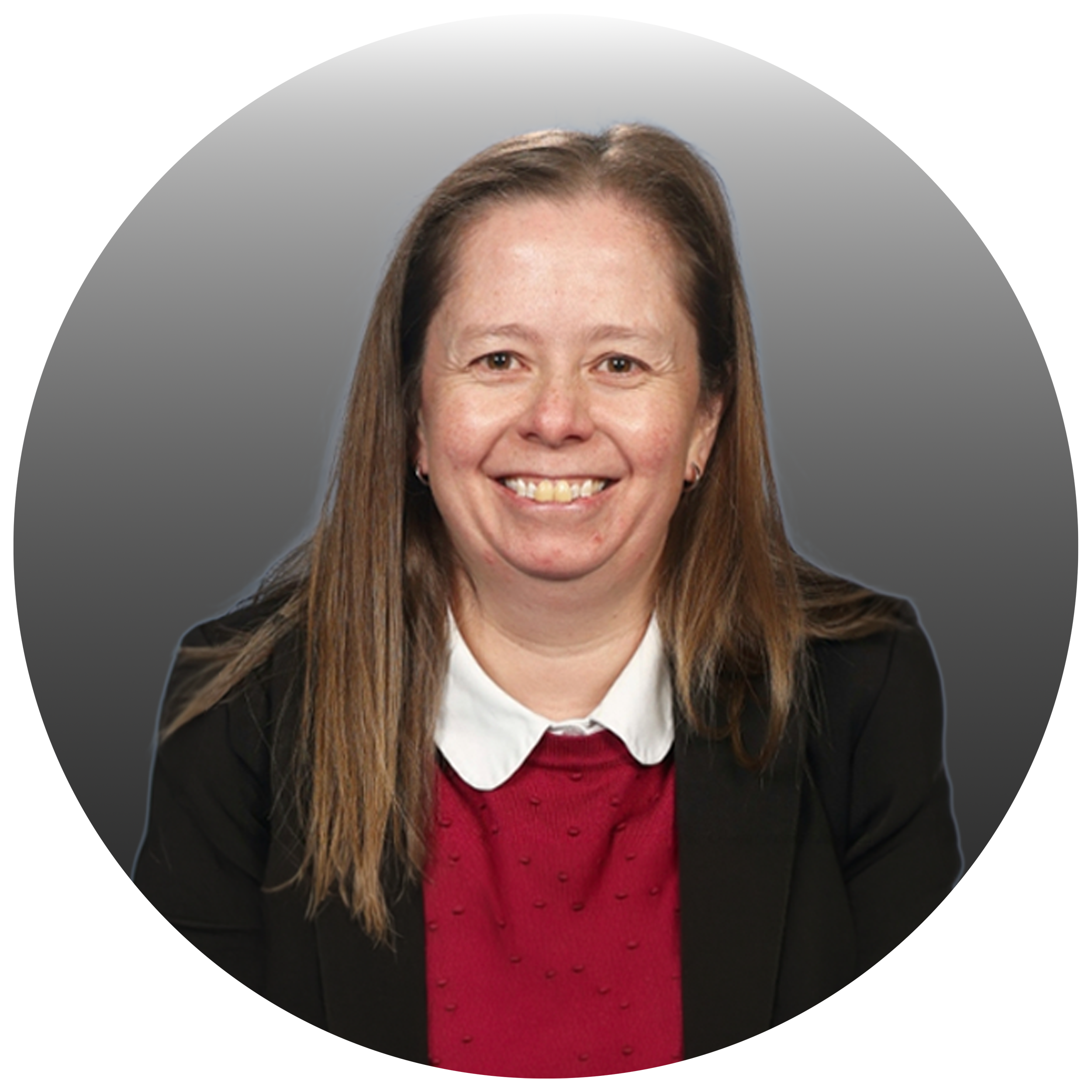 Smiling woman with shoulder-length brown hair, wearing a black blazer, white shirt, and red sweater, against a gray background.