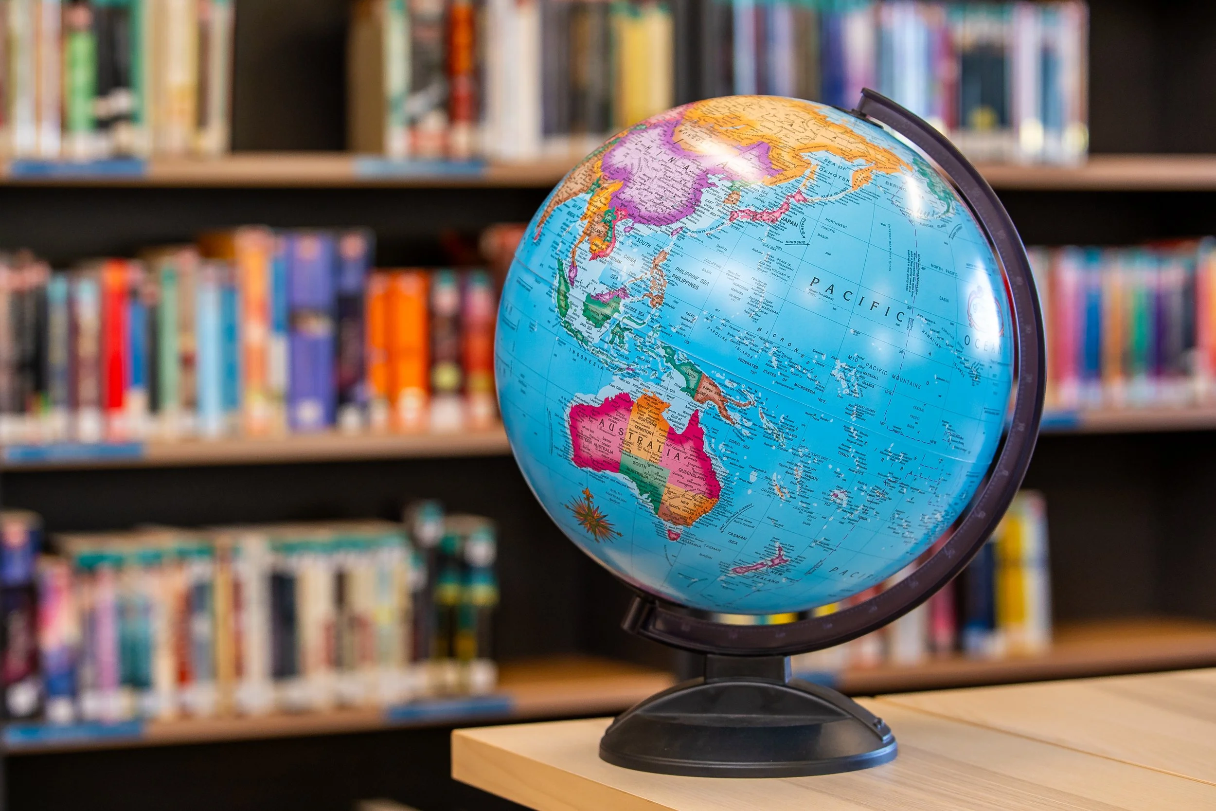 A globe on a wooden table with bookshelves in the background.