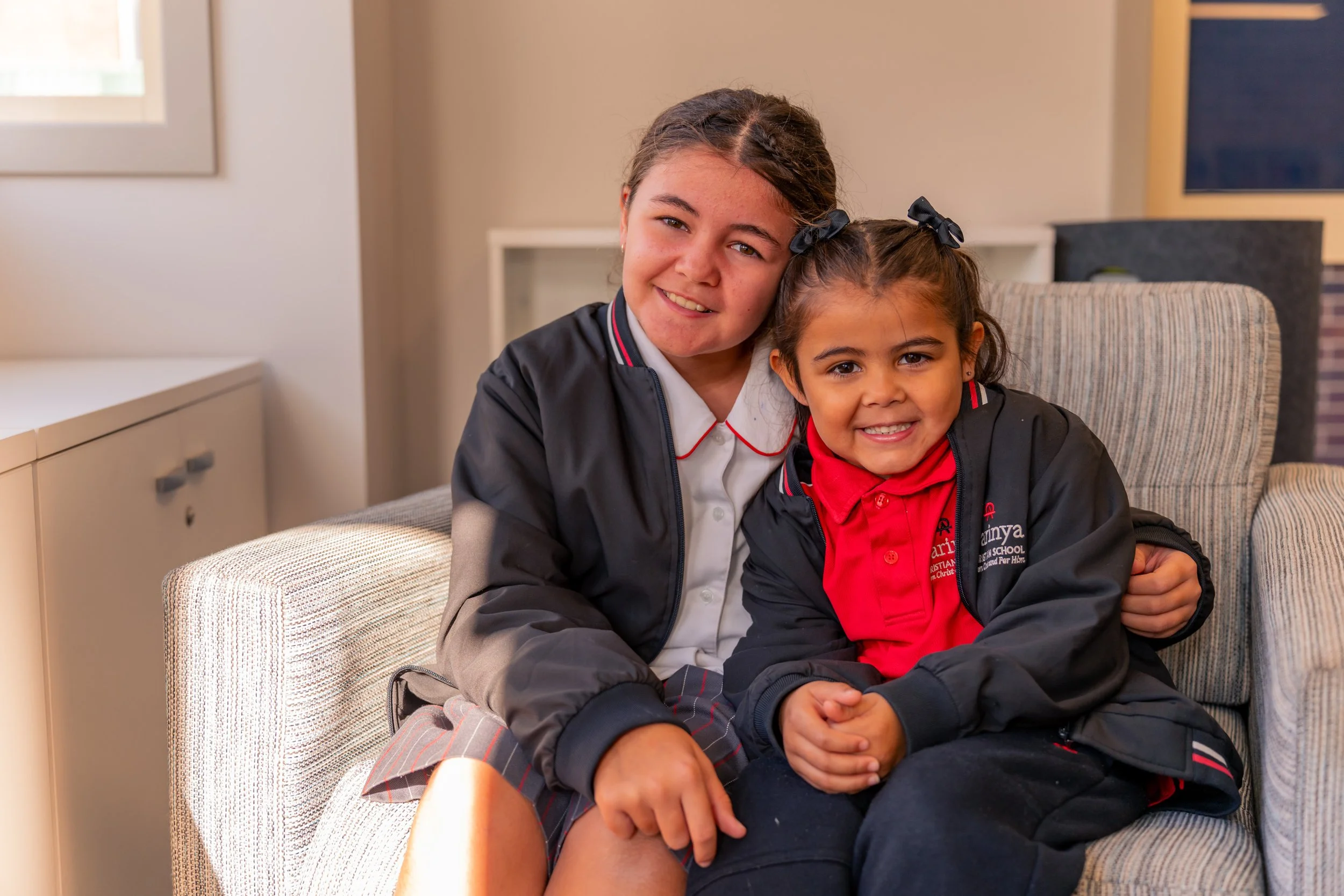 Two smiling students sitting together on a couch inside the Carinya Christian School, Gunnedah Library.