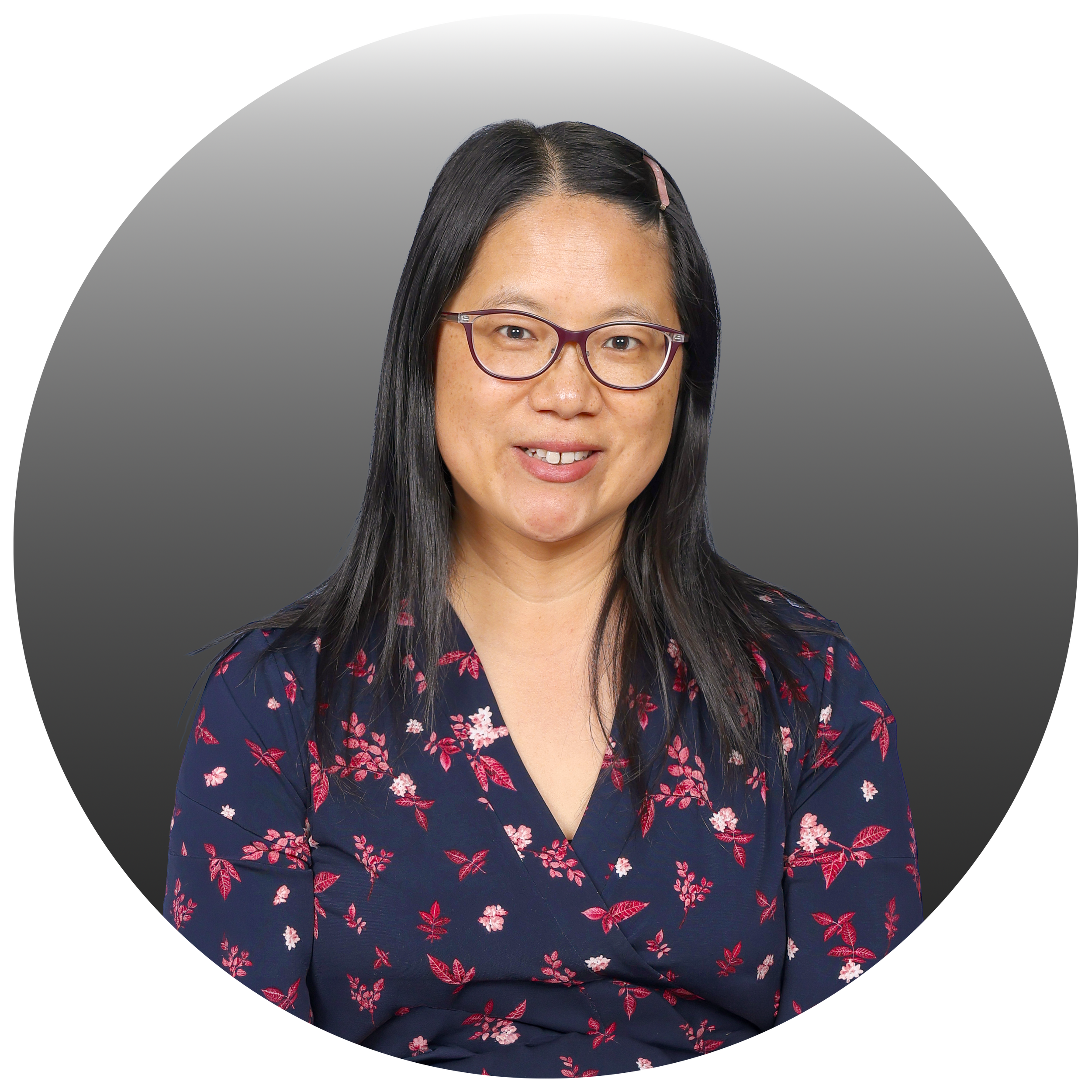 Headshot of an Asian woman with long black hair, glasses, and a pink hairpin, wearing a navy blue floral wrap dress, smiling against a gray background.
