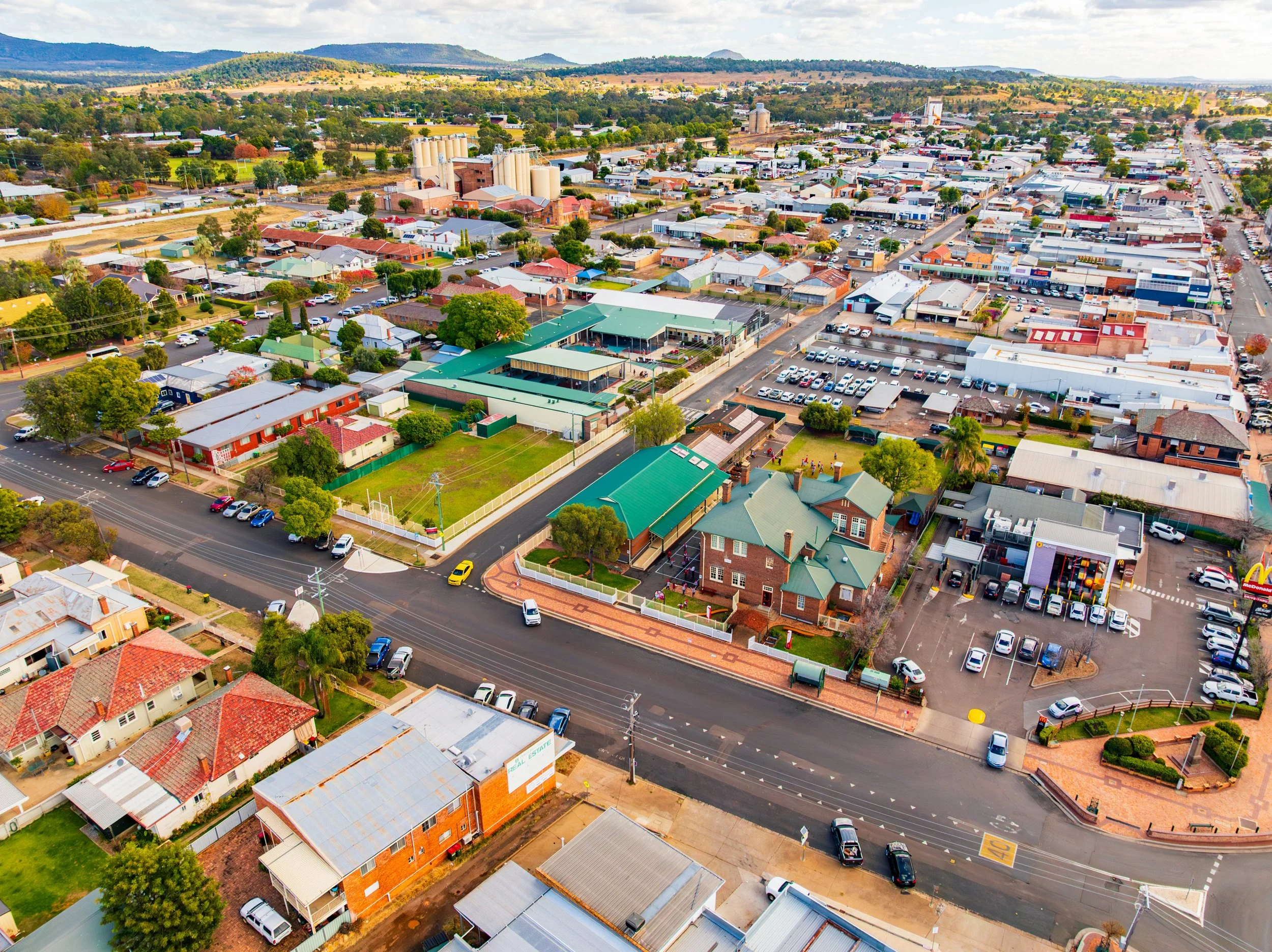 Aerial view of Carinya Christian School, Gunnedah, showing streets, houses, parking lots, a green building, and surrounding landscape with hills in the background.