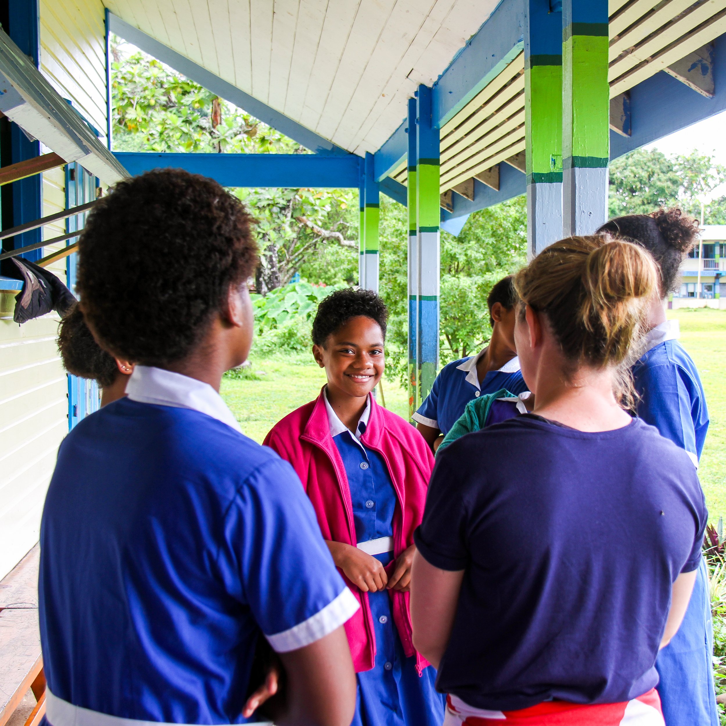 School group of students talking outside under a colorful sheltered walkway.