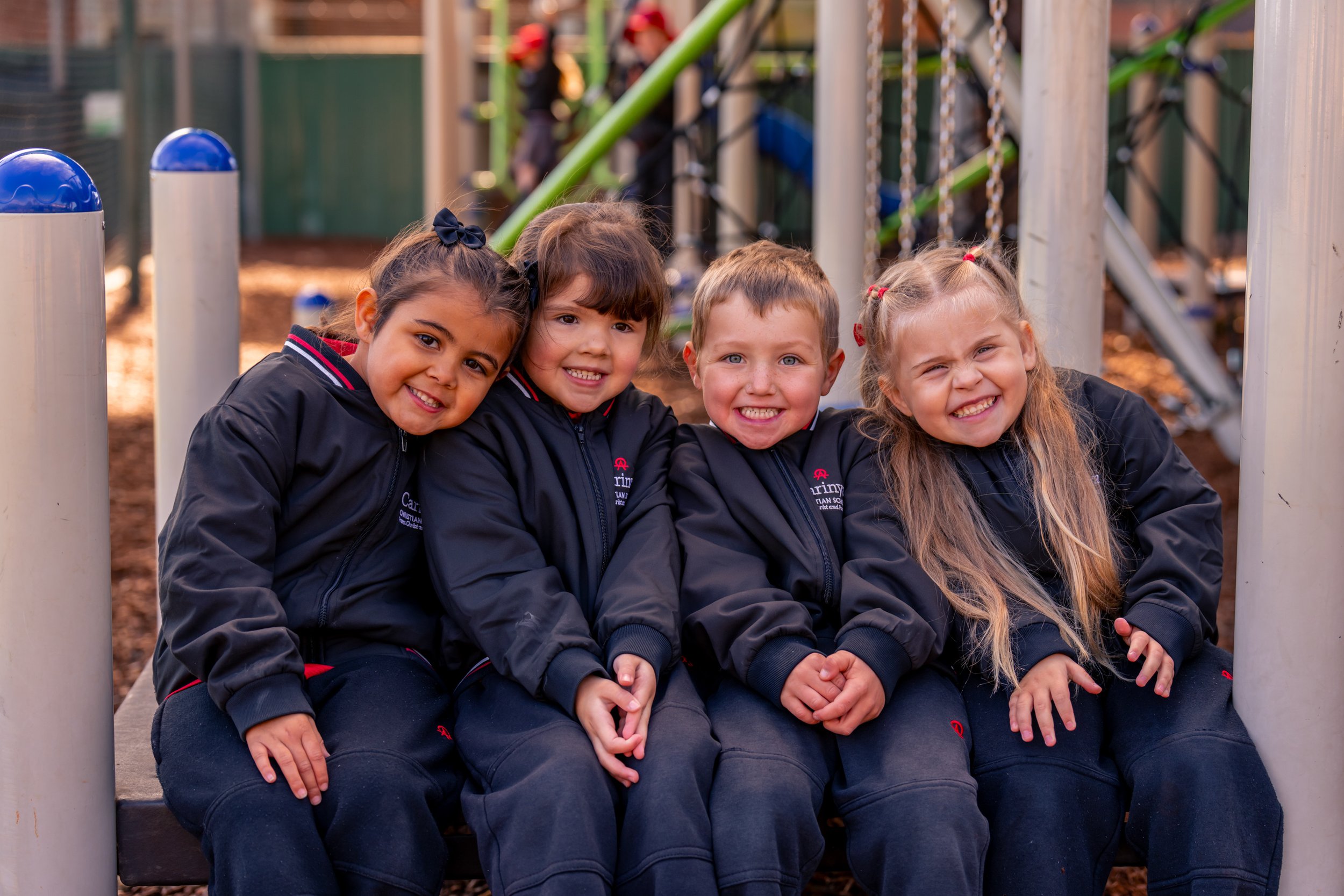 Four young children sitting together on a bench at a playground at Carinya Christian School, Gunnedah.