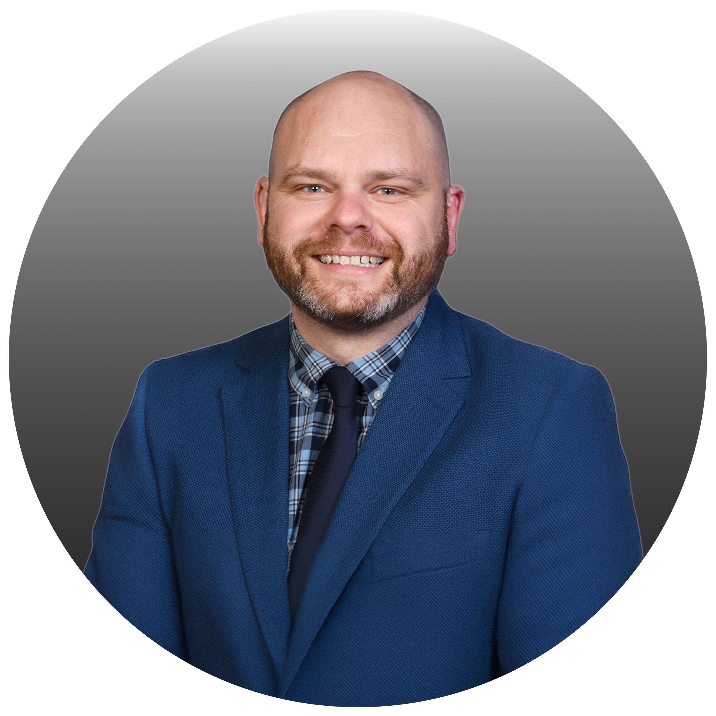 A professional man with a beard and bald head, wearing a blue suit, checkered shirt, and navy tie, smiling in front of a gray gradient background.