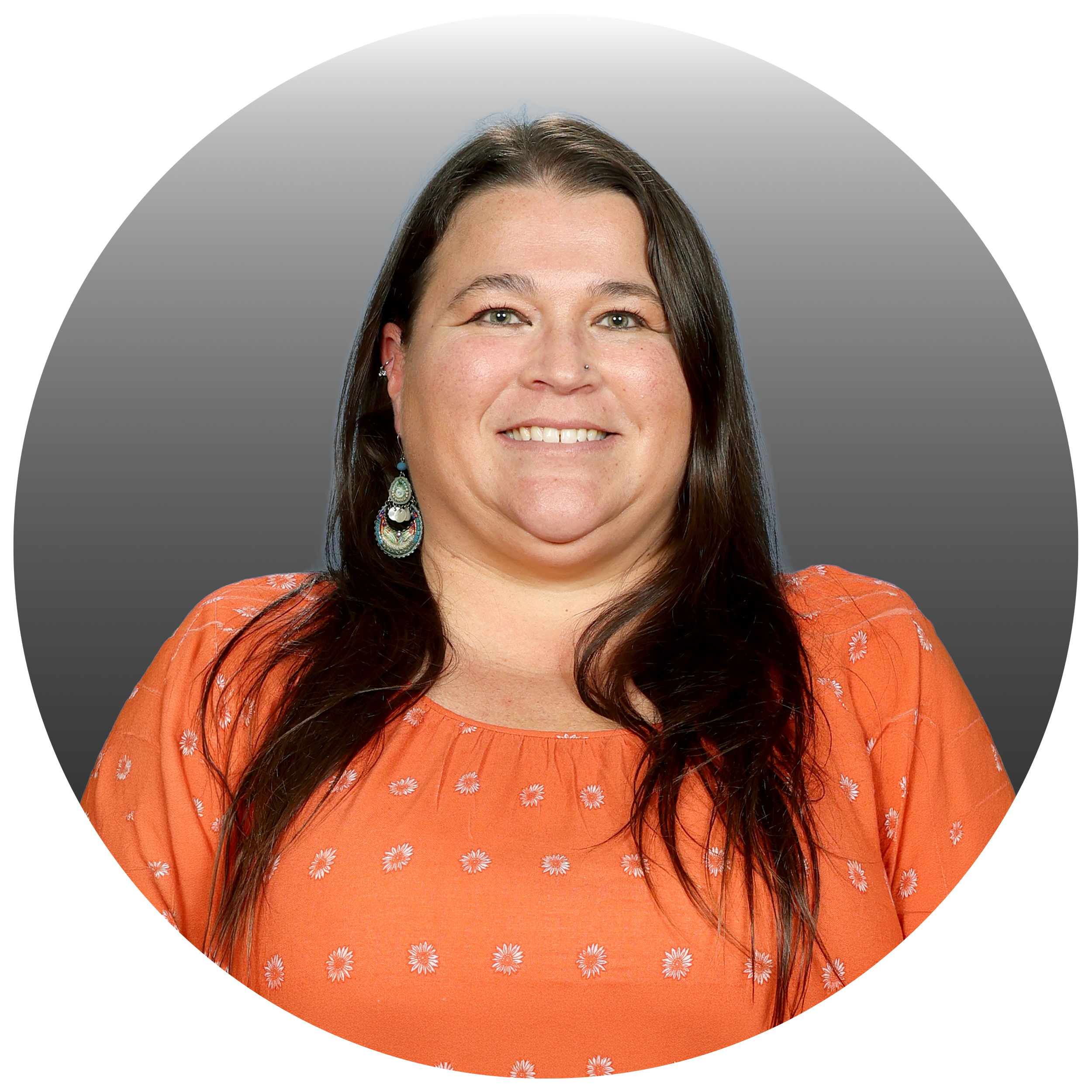 A woman with long brown hair, blue eyes, and earrings, smiling, wearing an orange top with small white floral patterns.