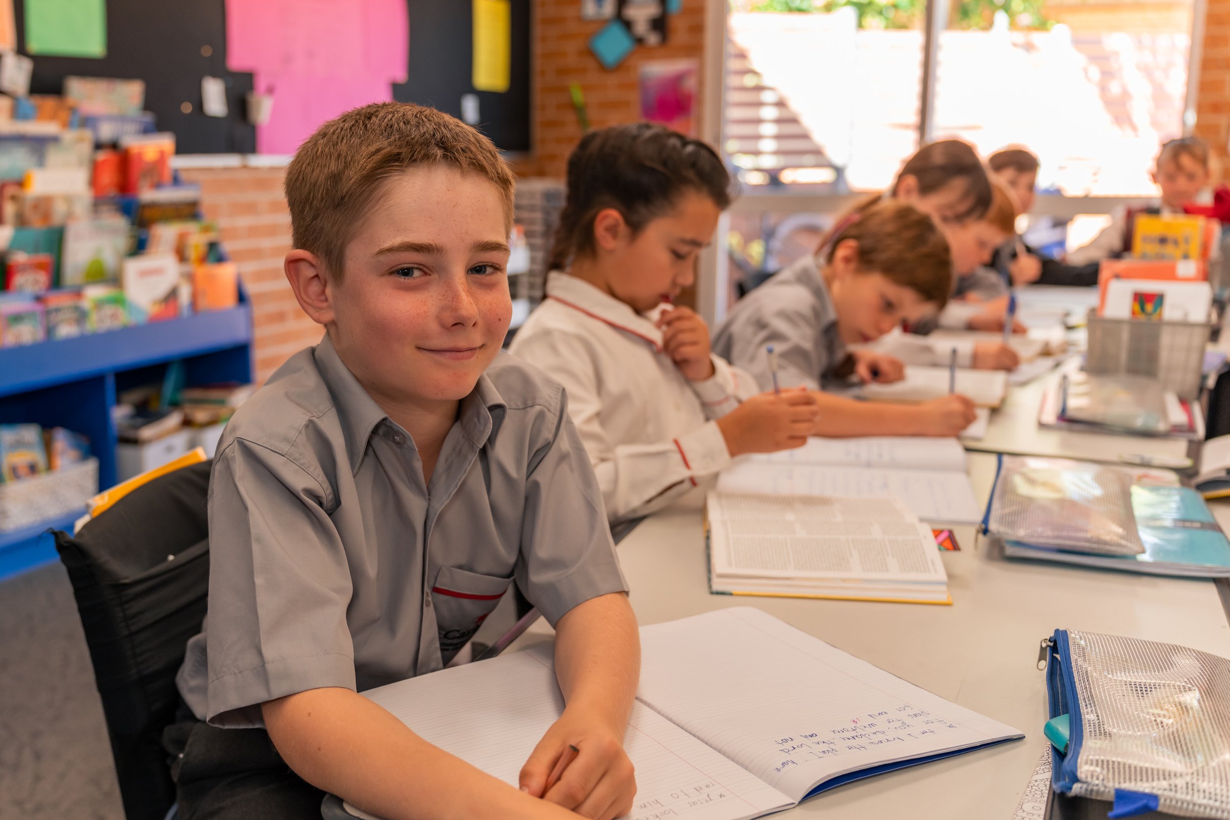 A male Junior School Student inside a classroom, with other students in the background at Carinya Christian School, Tamworth.