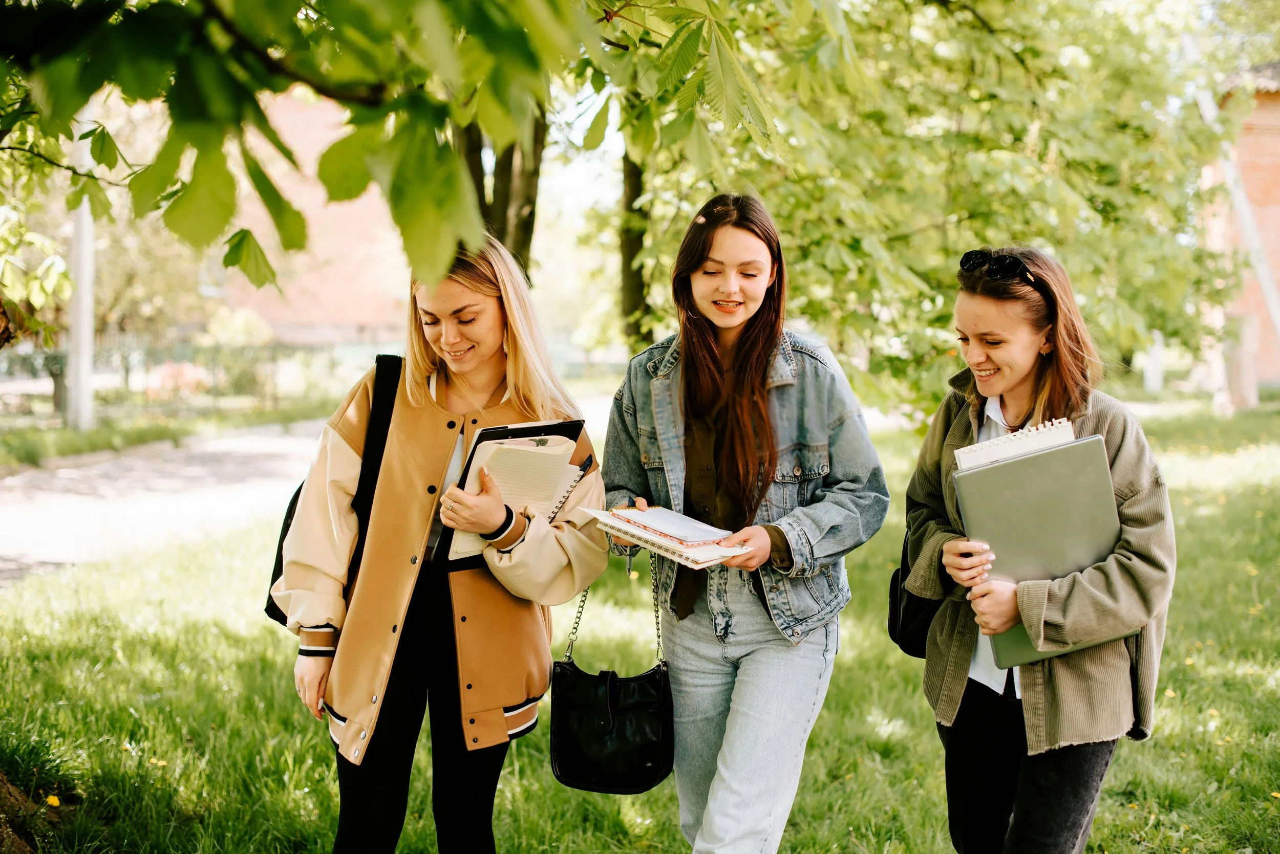 Trois jeunes femmes marchant dans un parc verdoyant, tenant des livres et des cahiers.