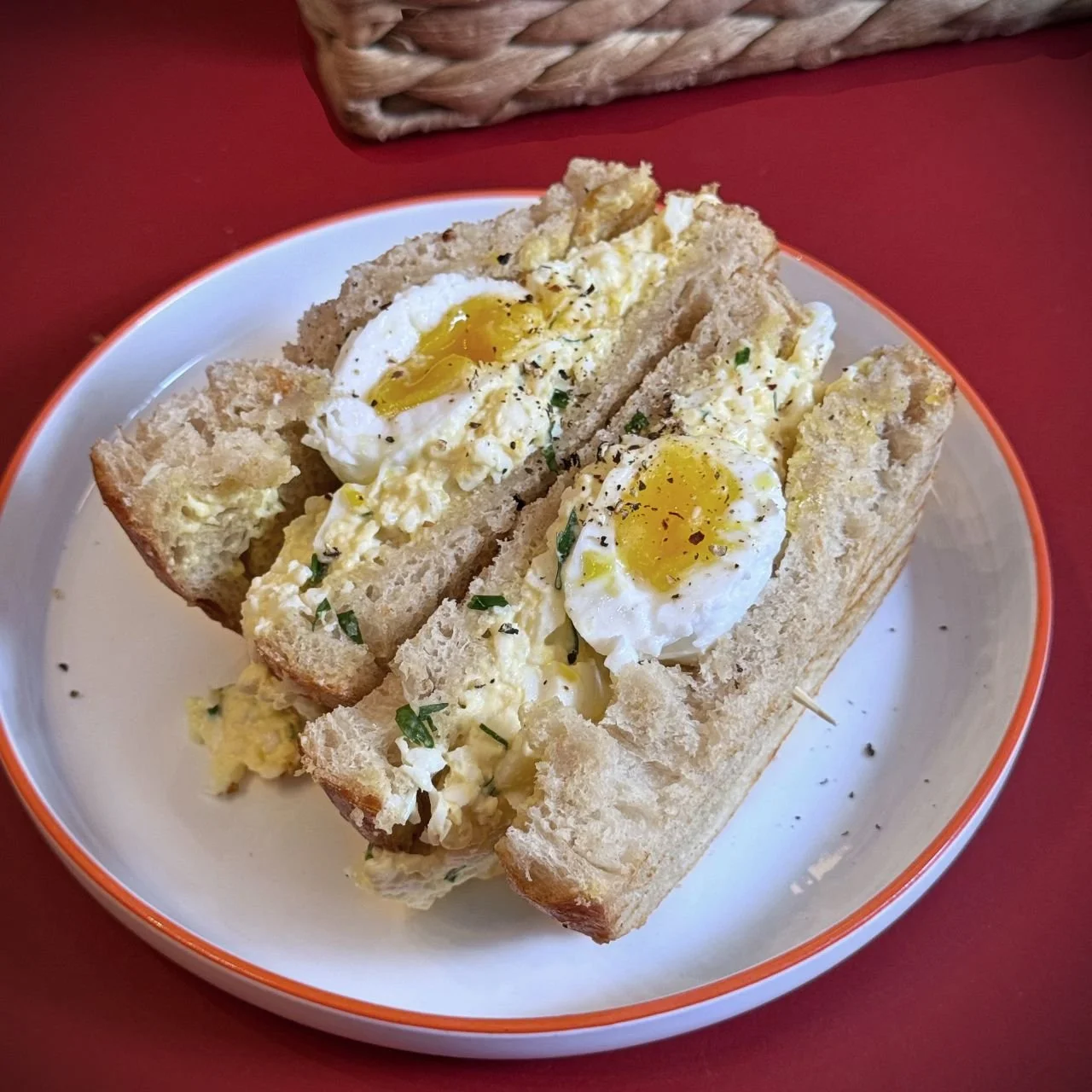 Fresh egg sandwich on brioche bread with creamy egg salad and halved soft-boiled egg, served on a white plate with red rim at Café Helma in Munich