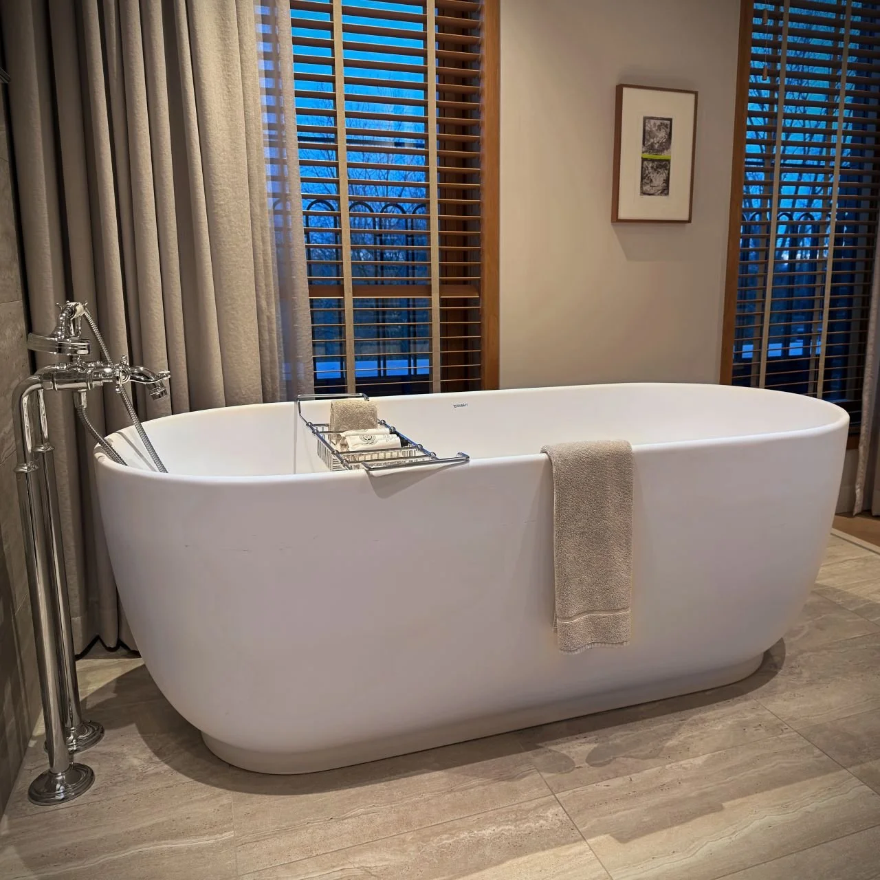 Freistehende weiße Badewanne mit Armatur in einer Hotelsuite des Pillows Hotels in Amsterdam vor einem Fenster mit Holzjalousien.