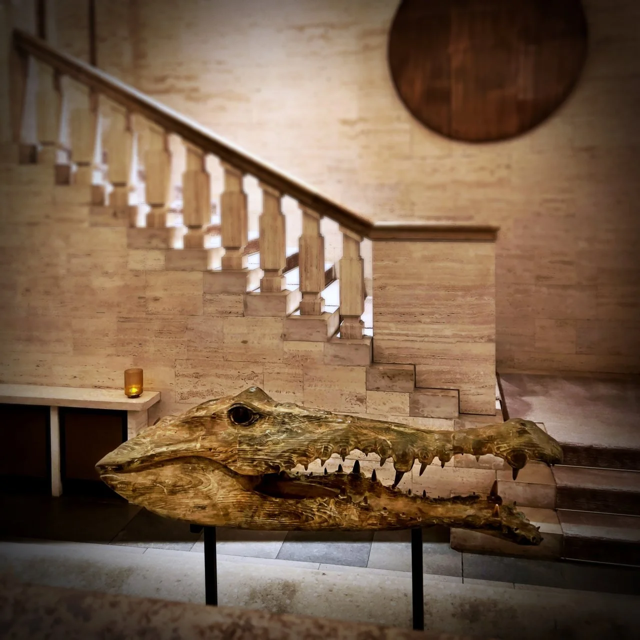 In der Lobby des Hotels Das Stue in Berlin steht eine große Krokodil Skulptur von Quentin Garel aus Holz auf einem Sockel. Dahinter führt eine breite Steintreppe mit Balustrade zu einer Galerie im oberen Bereich.