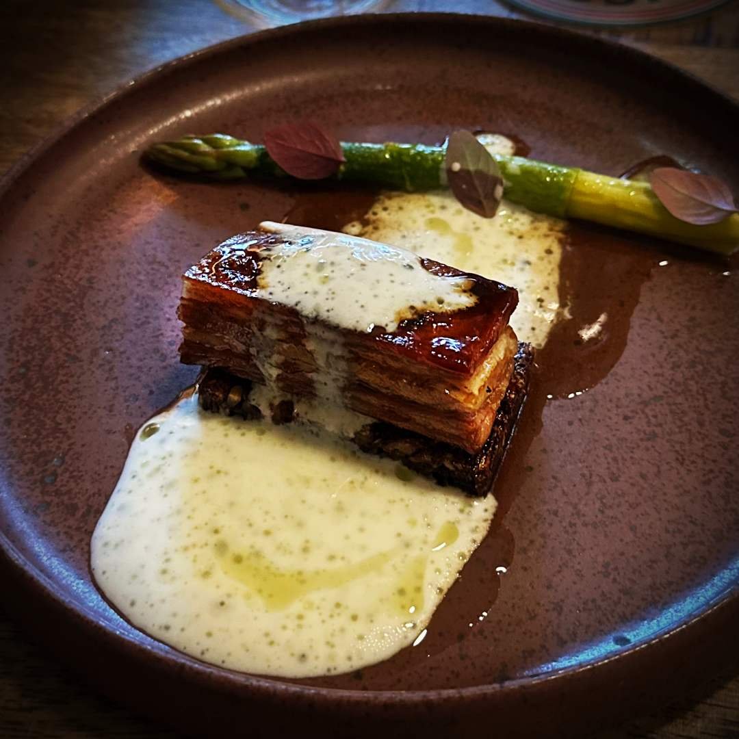 Gegrilltes Lamm mit grünem Spargel und einer Kefir-Sauce im Restaurant Selma in Kopenhagen. Das geschichtete Fleisch wird auf einem dunklen Keramikteller serviert.