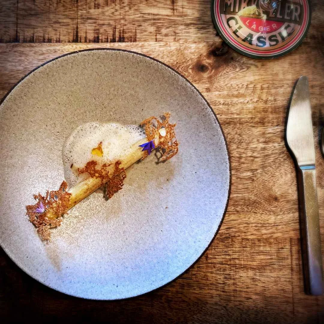 Weißer Spargel mit Bay Shrimps und Schaum auf einem Keramikteller im Restaurant Selma in Kopenhagen. Daneben liegen Besteck und ein Mikkeller-Bierdeckel auf dem Holztisch.