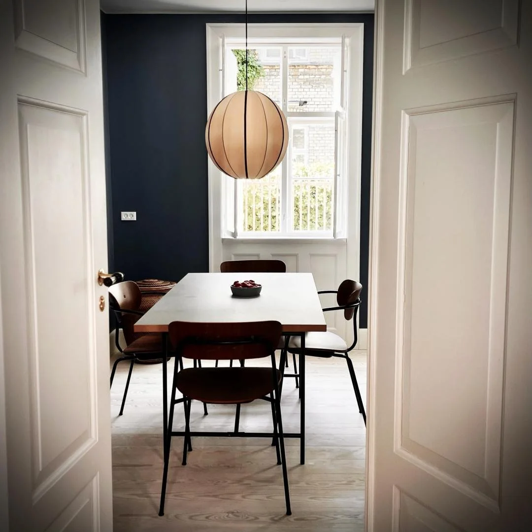 The dining room of an Airbnb on Haregade in Copenhagen, viewed through an open white door. The room features a table, chairs, and a round pendant lamp