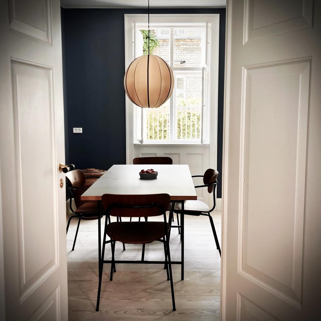 Das Esszimmer eines Airbnb in der Haregade in Kopenhagen, gesehen durch eine offene weiße Tür. Im Raum stehen ein Tisch, Stühle und eine runde Hängelampe