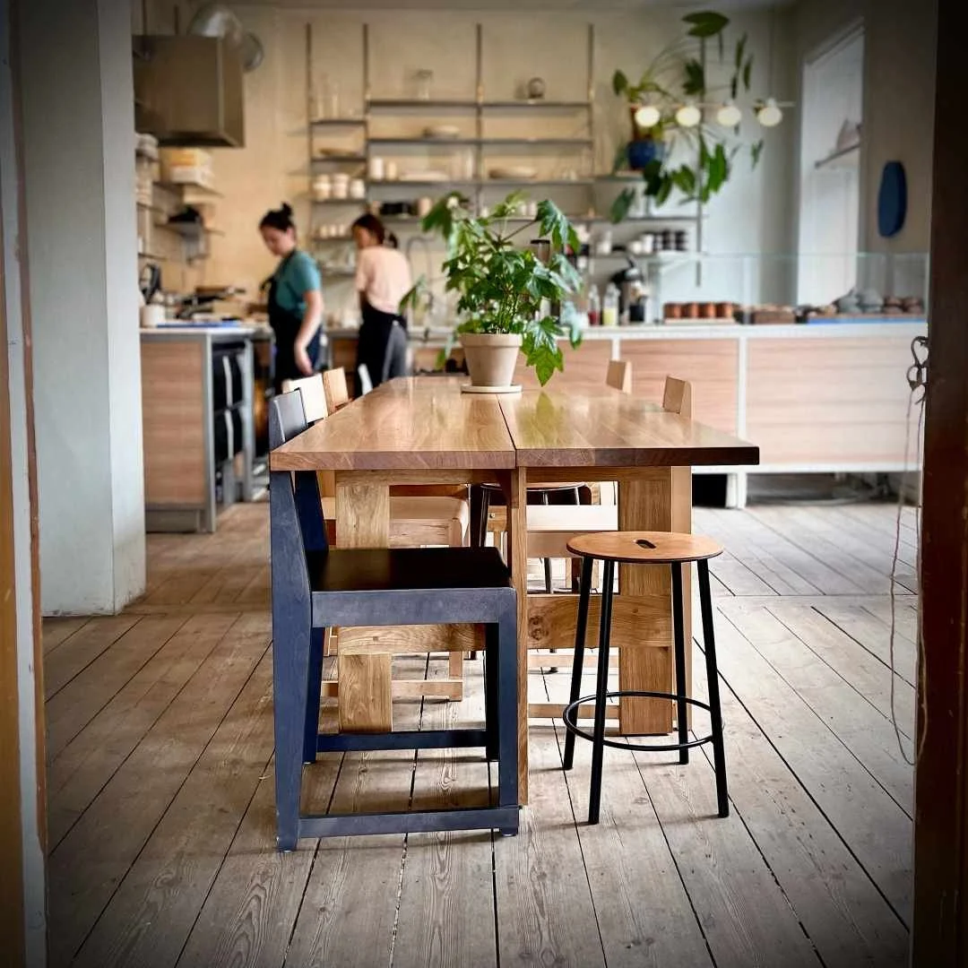 Interior of Apotek 57 café in Copenhagen showing a wooden communal table and staff working in the open kitchen background.