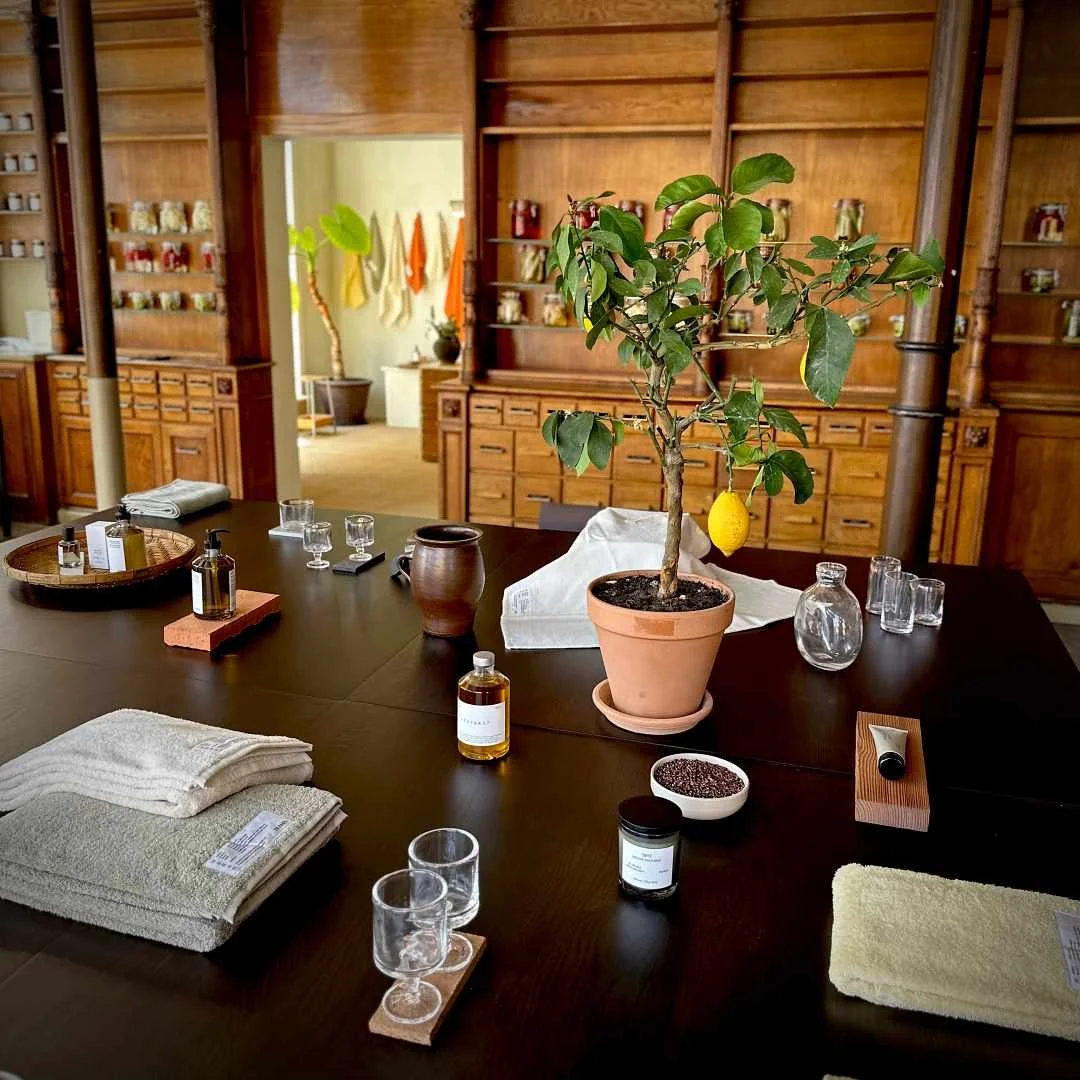 A wooden table at Frama Studio Store (Apotek 57) in Copenhagen featuring a lemon tree, towels, and skincare products in front of wooden shelves.