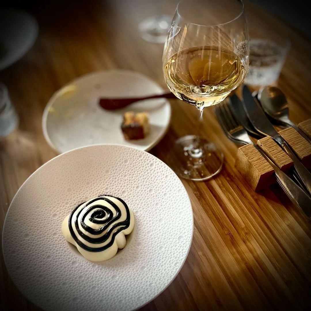 Eine Vorspeise aus weisser Beete mit dekorativer Lakritz-Spirale, angerichtet in einer strukturierten weißen Schale im Ja Restaurant in Amsterdam, dazu ein Glas Weißwein.