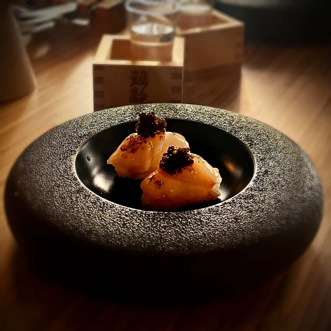 Zwei mundgerechte Häppchen mit Kaviar auf schwarzem Teller mit breitem Rand, serviert auf einem Holztisch im Restaurant Jā in Amsterdam.